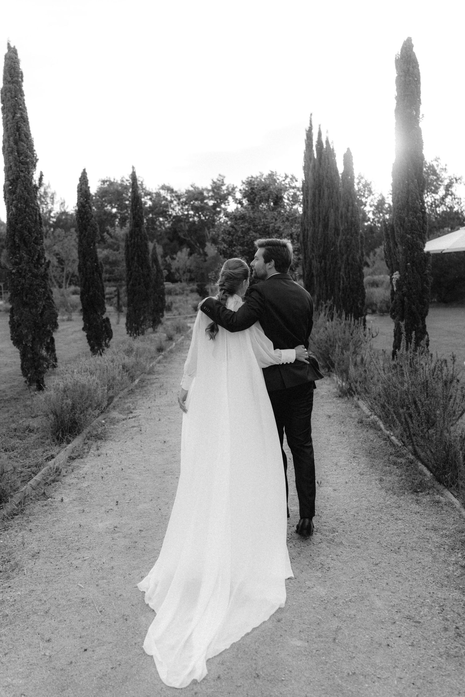 Black and white photo of couple walking down cypress tree-lined path.