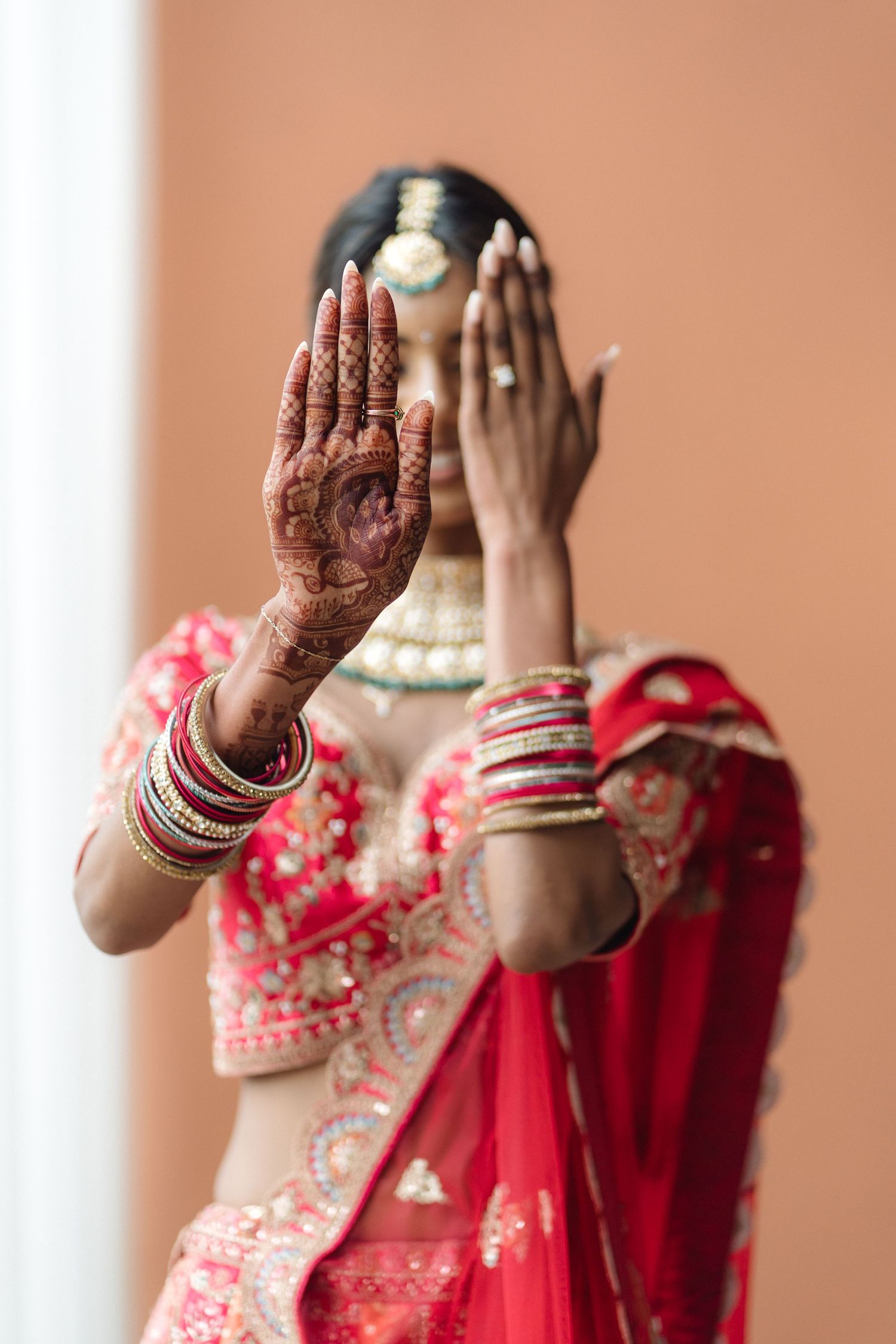 Decorated hands with intricate henna designs and traditional red bridal attire.