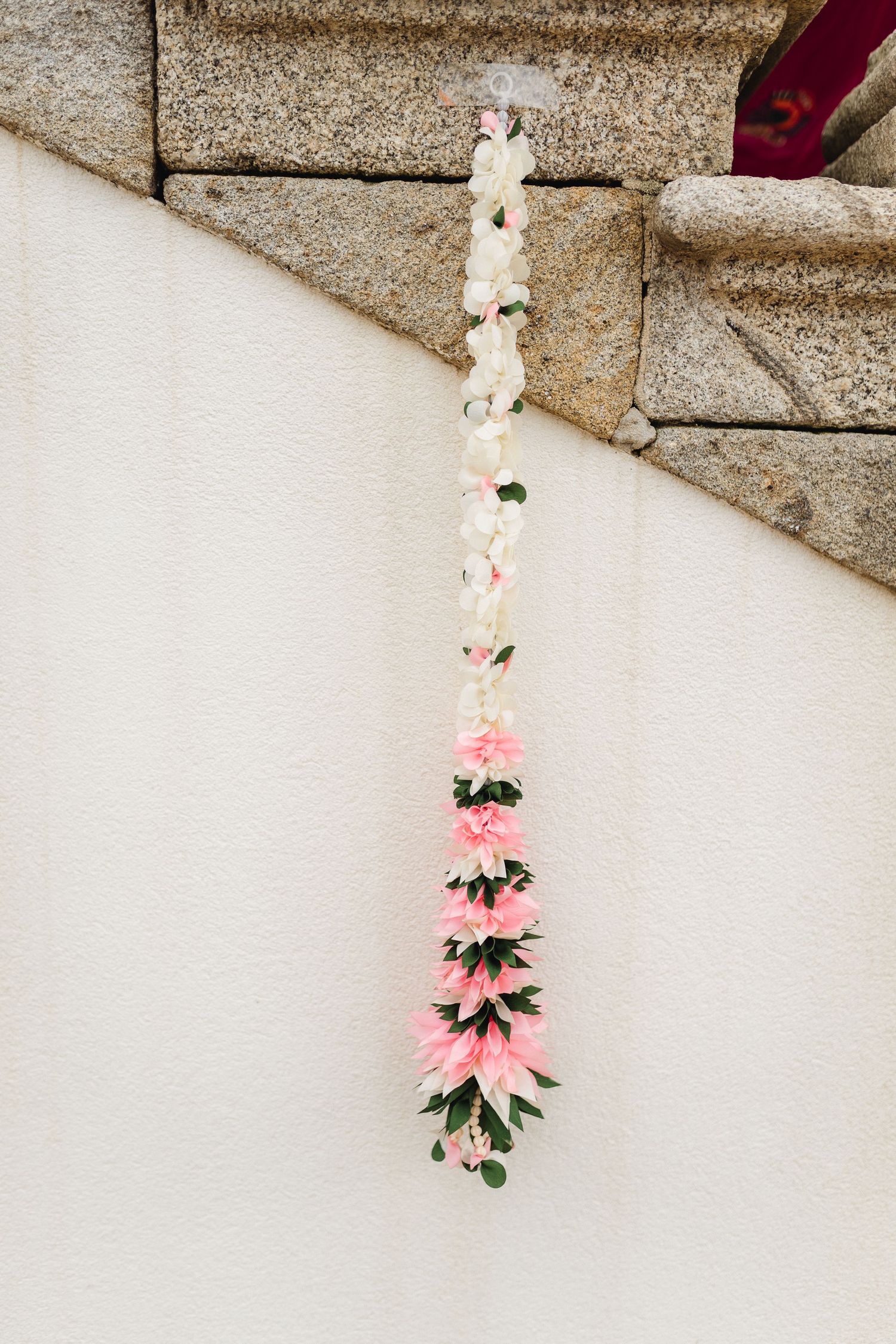 Pink and white floral decorative hanging garlands against a stone wall background.