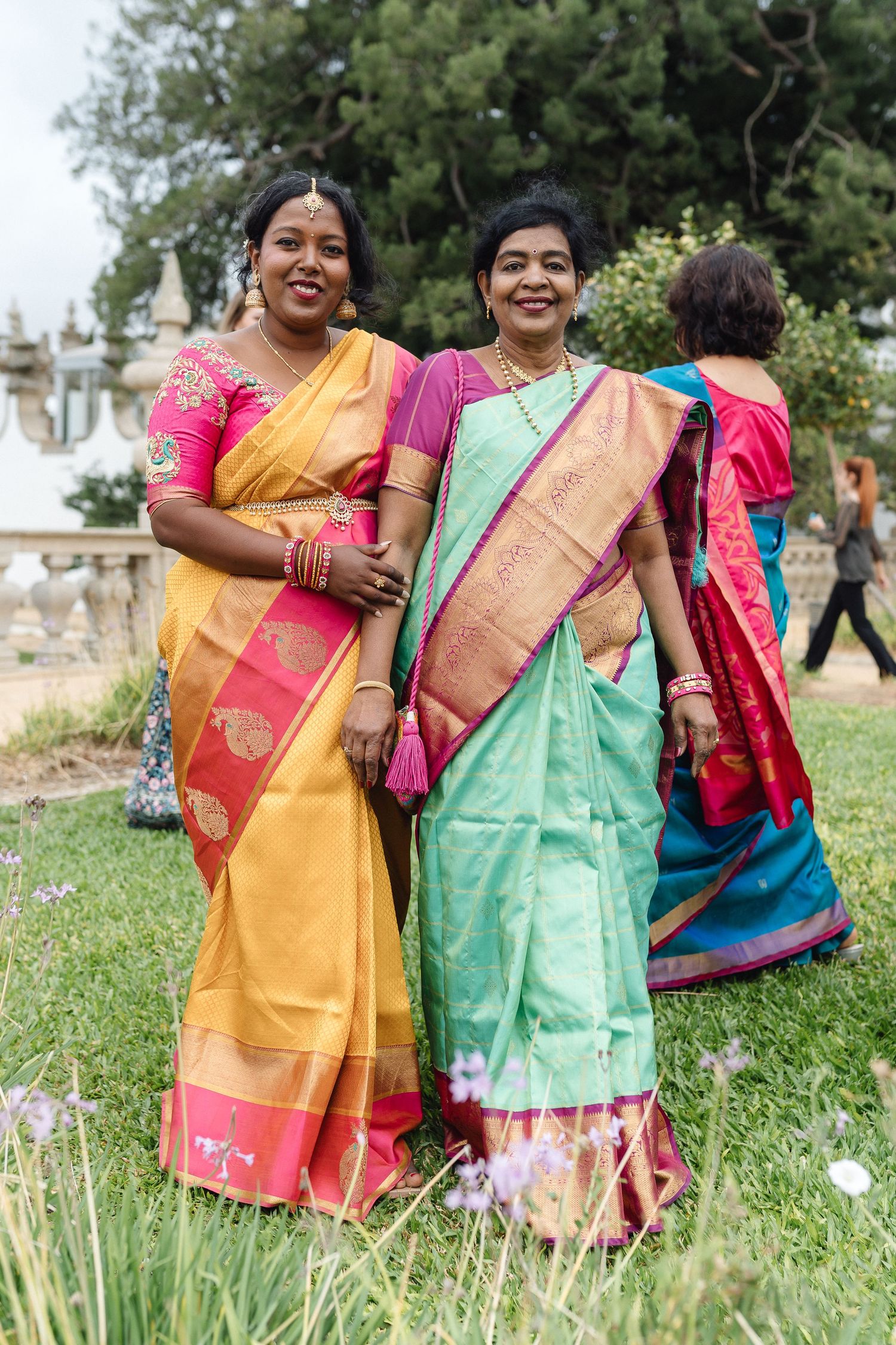 Women wearing colorful traditional Indian saris in yellow, green, and pink standing together in a garden.