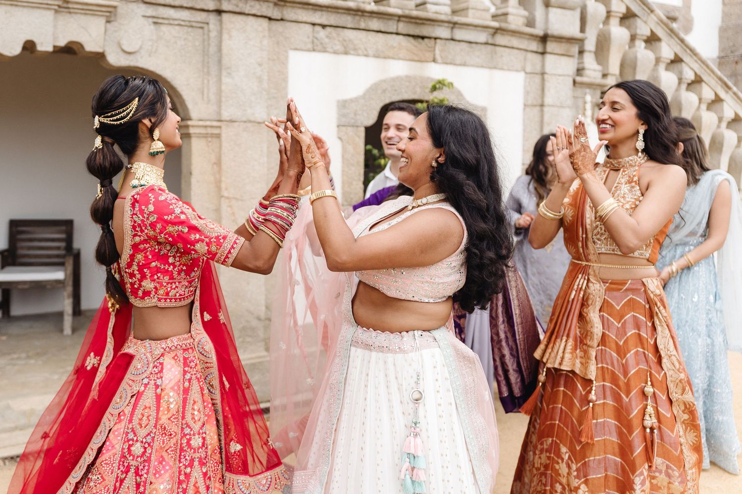Wedding party members in vibrant lehengas and formal wear gather for photos.