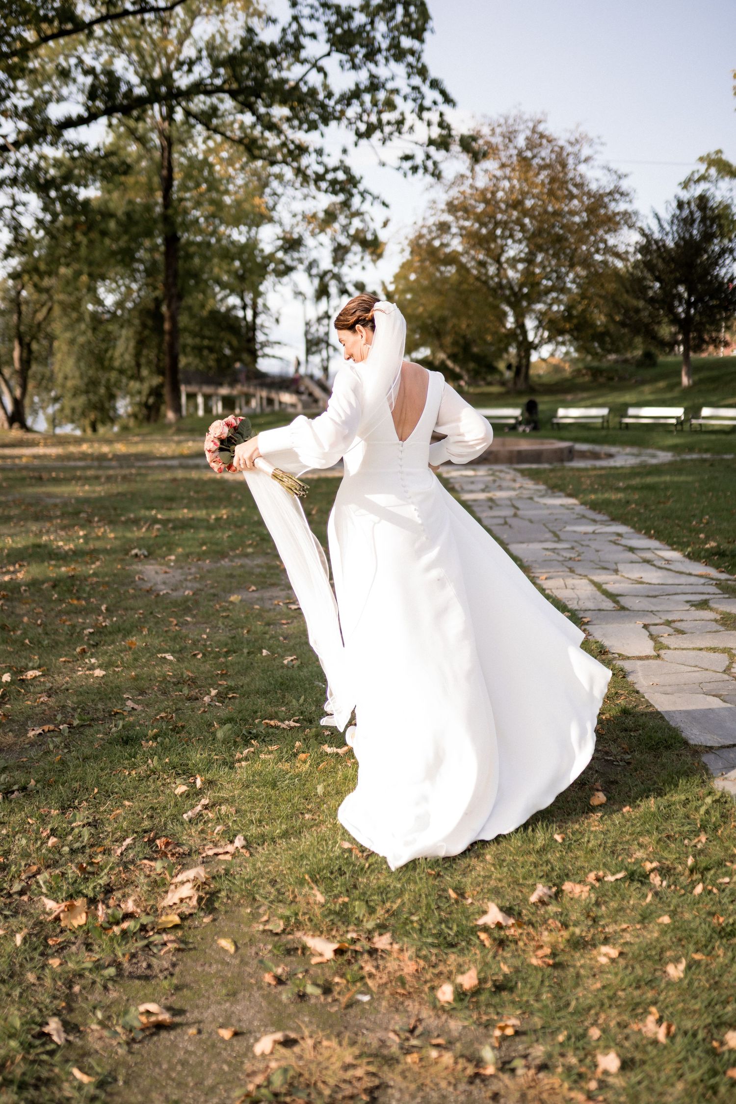 A flowing white dress twirls gracefully along a stone pathway surrounded by autumn leaves.