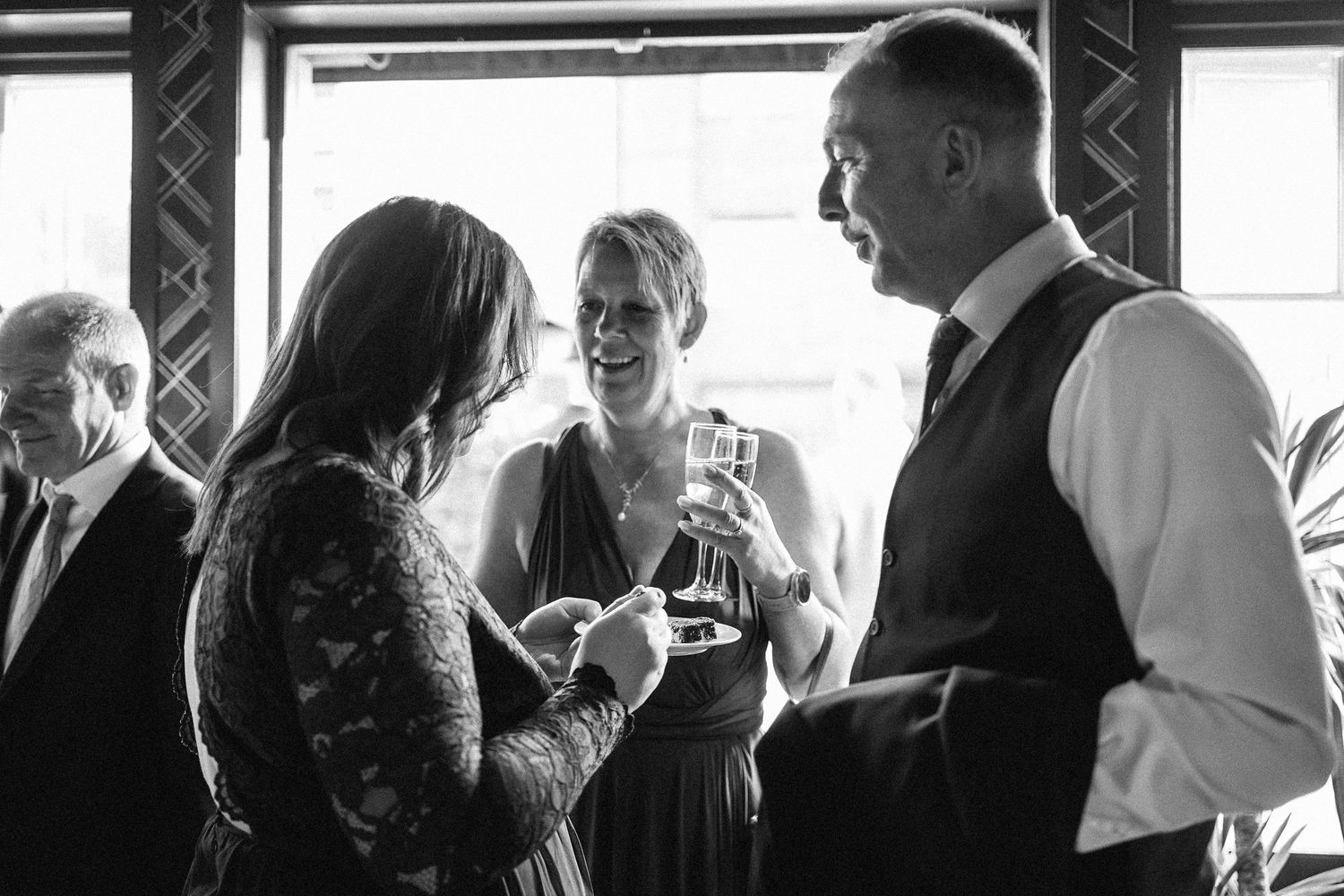 Black and white candid photo of wedding guests enjoying conversation at a reception.