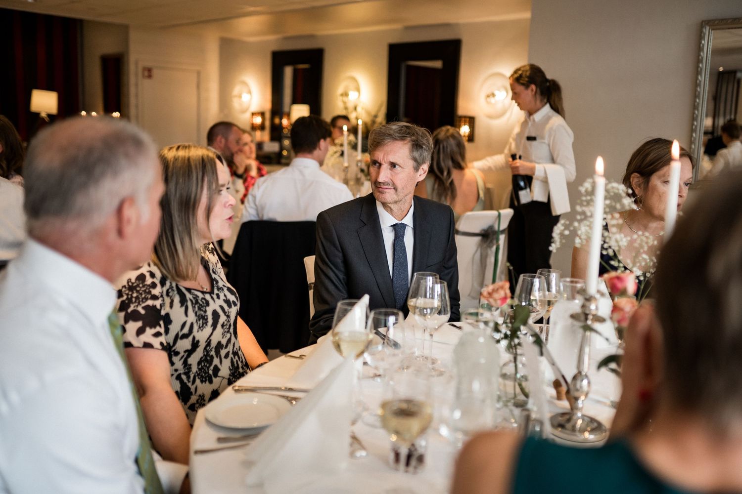 Elegant wedding reception dinner with candlelit tables and guests socializing.