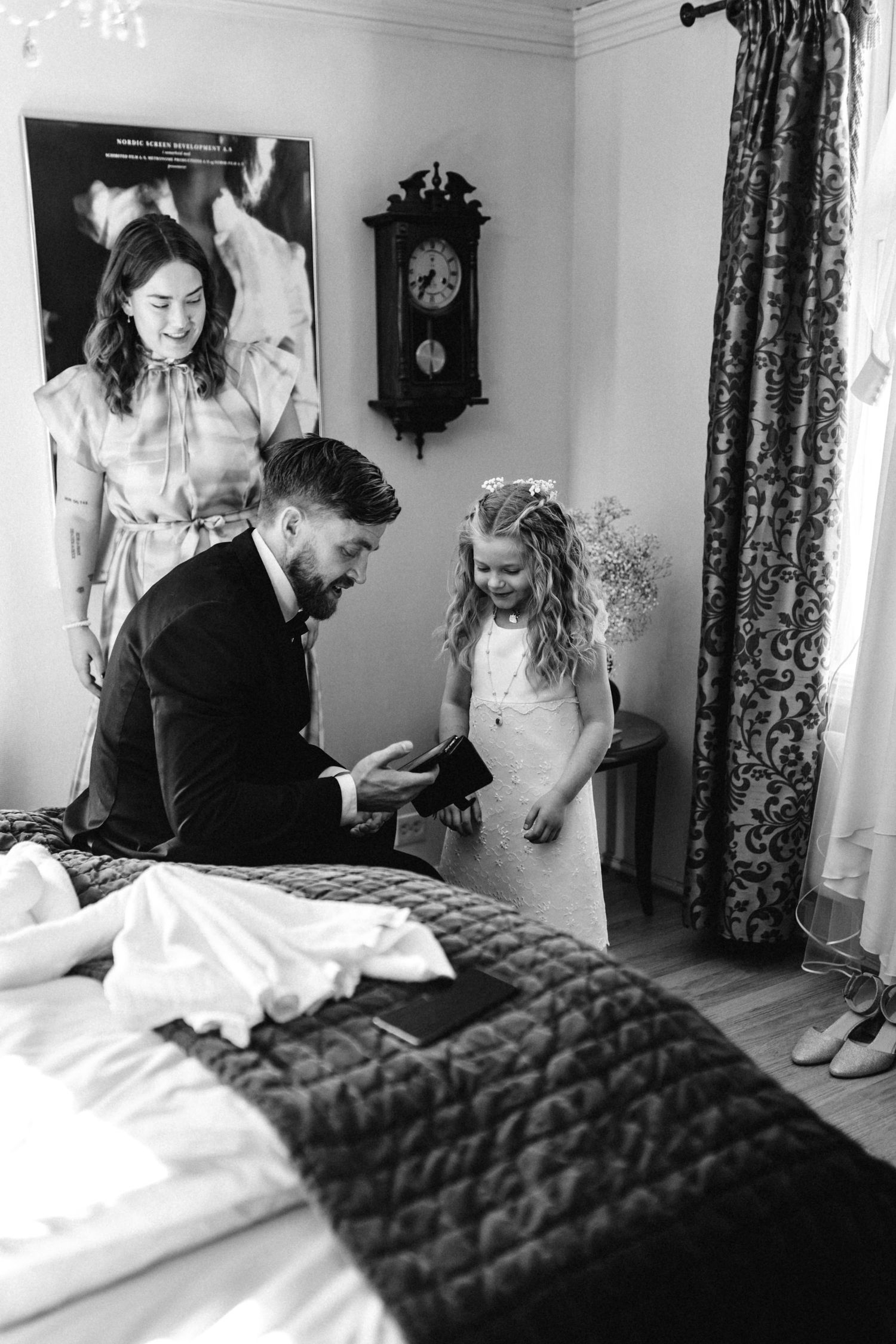 Black and white photo showing final dress preparations in a bedroom with floral curtains.