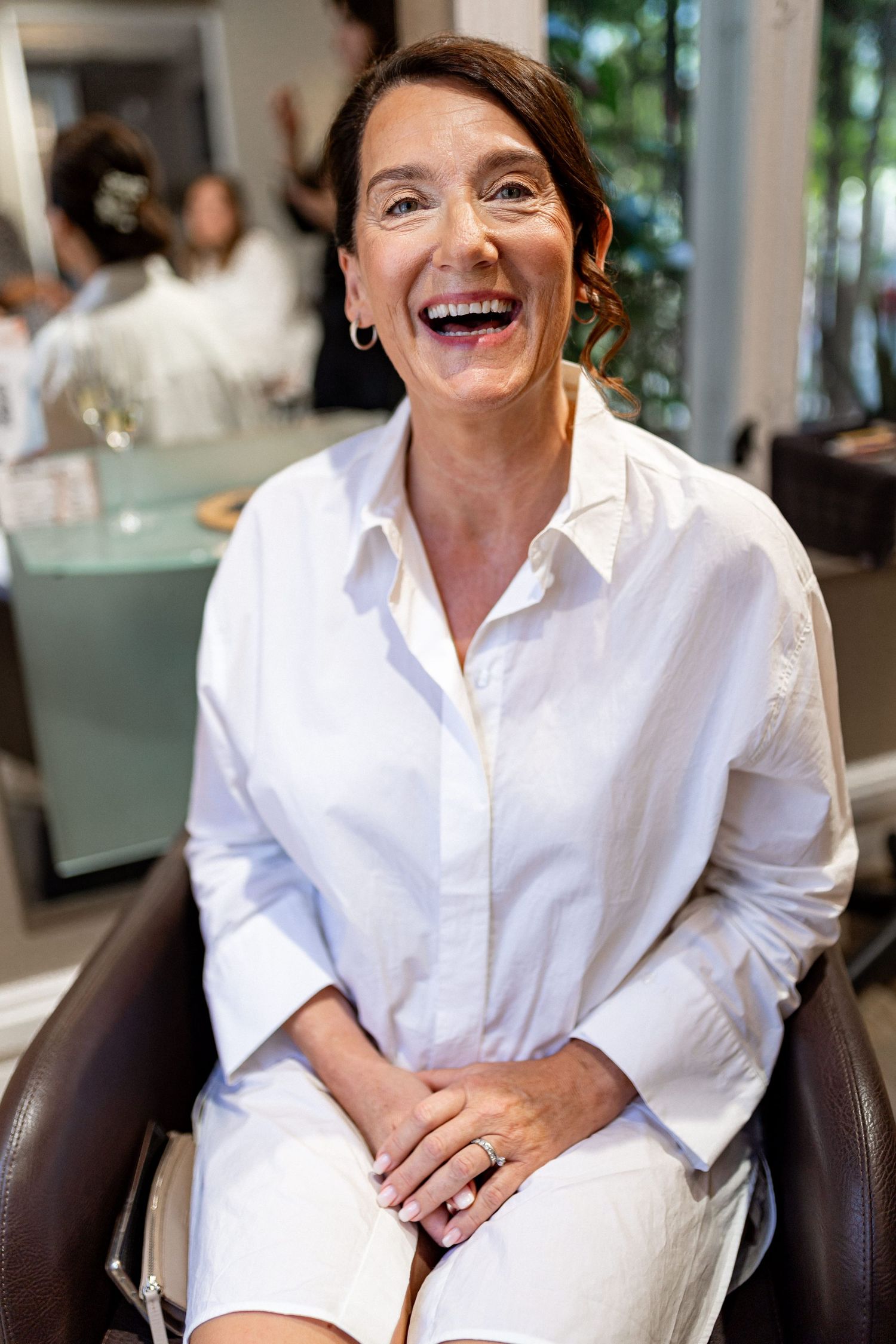 Person in white button-down shirt sitting and laughing in an indoor setting.