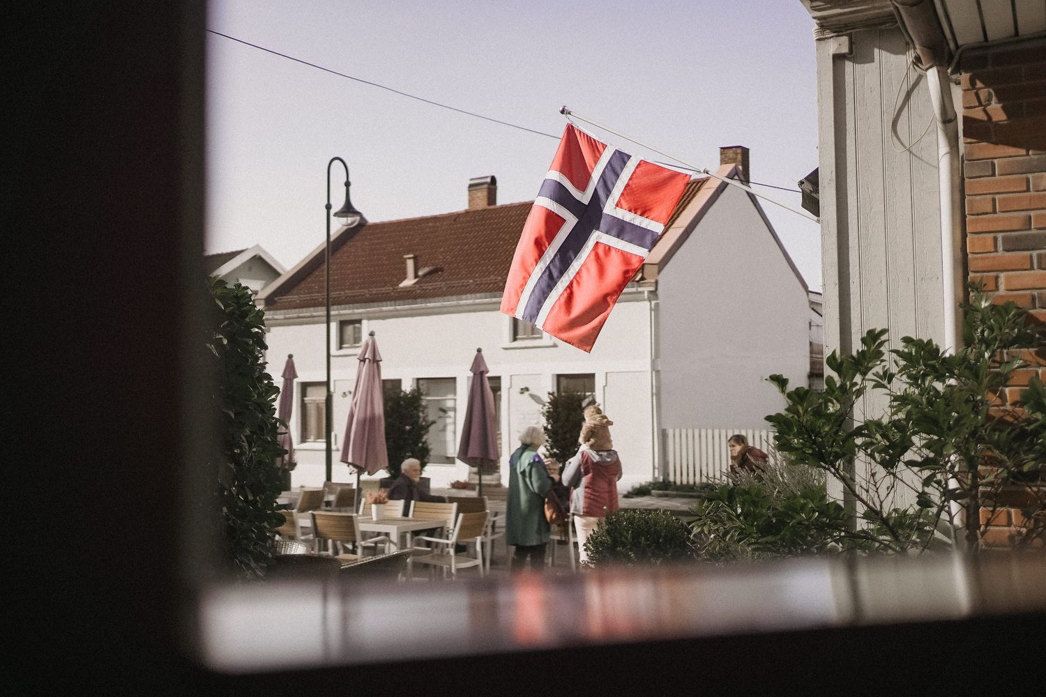 Norwegian flags wave against a white house exterior on a cloudy day.