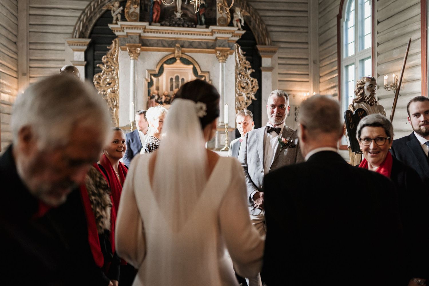 Wedding ceremony in a white-paneled church with guests seated and ornate decor visible.