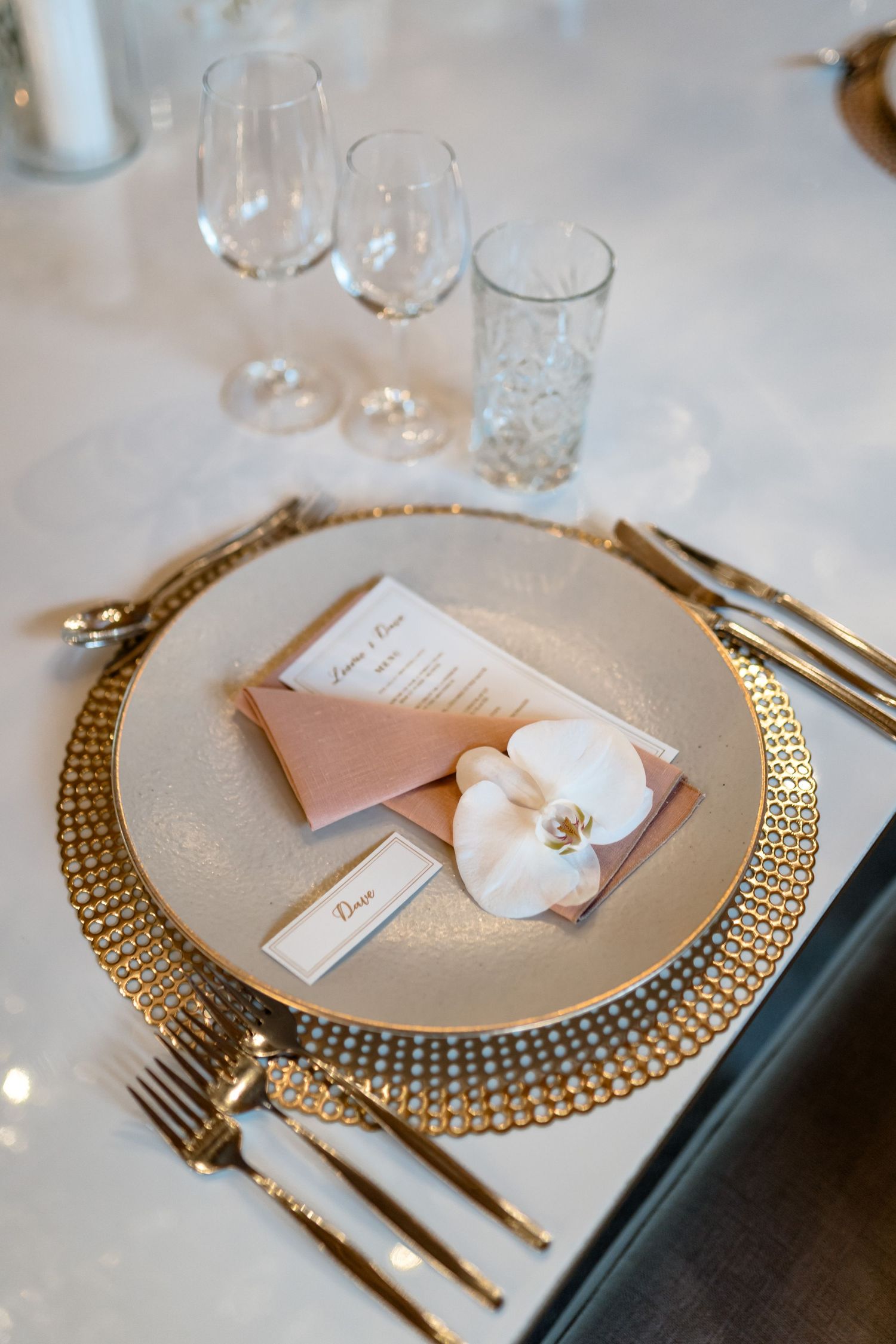 An elegant place setting with gold charger plate, crystal glasses, and white orchid decoration.