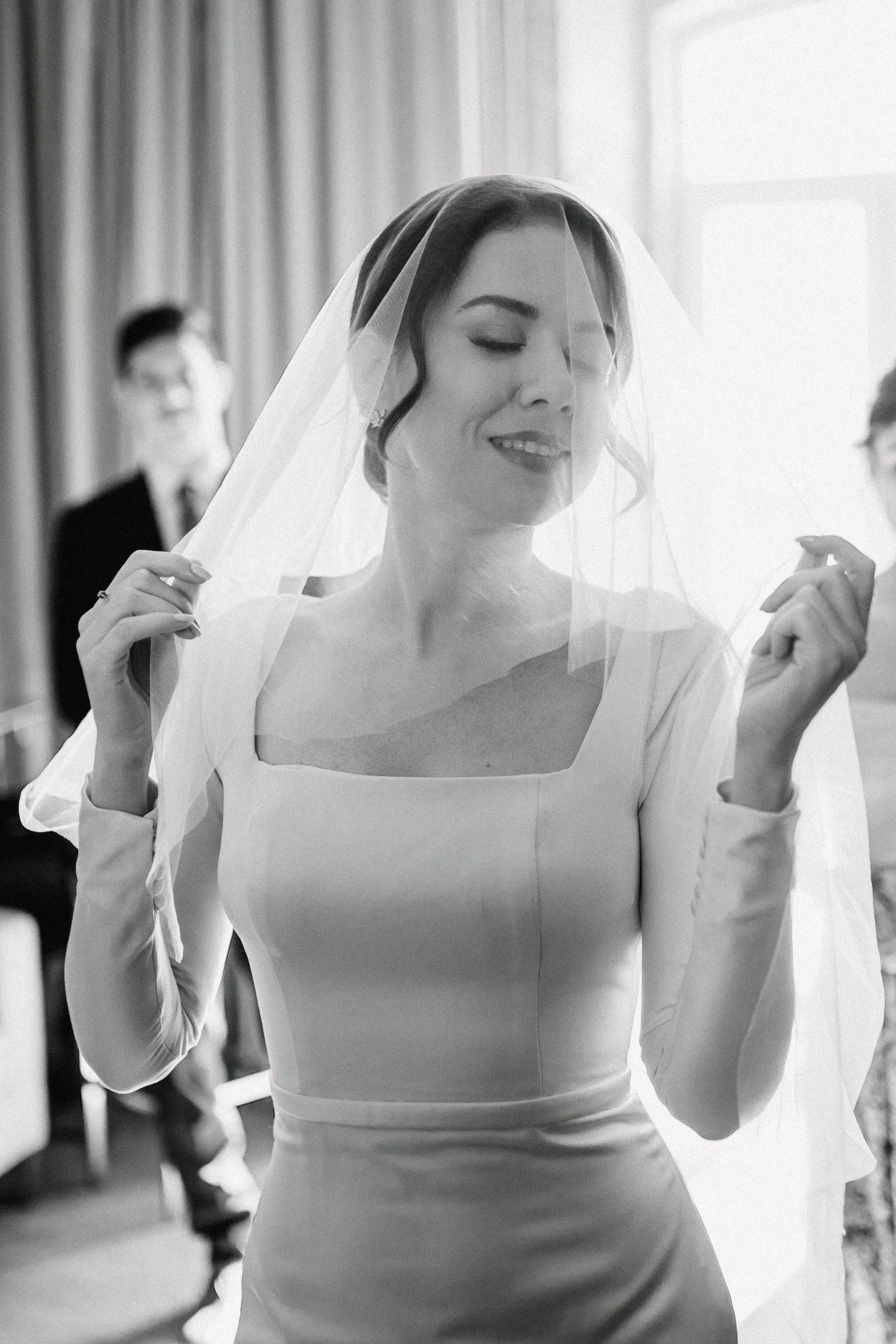 Candid moment of bride in modern square neck dress adjusting veil.