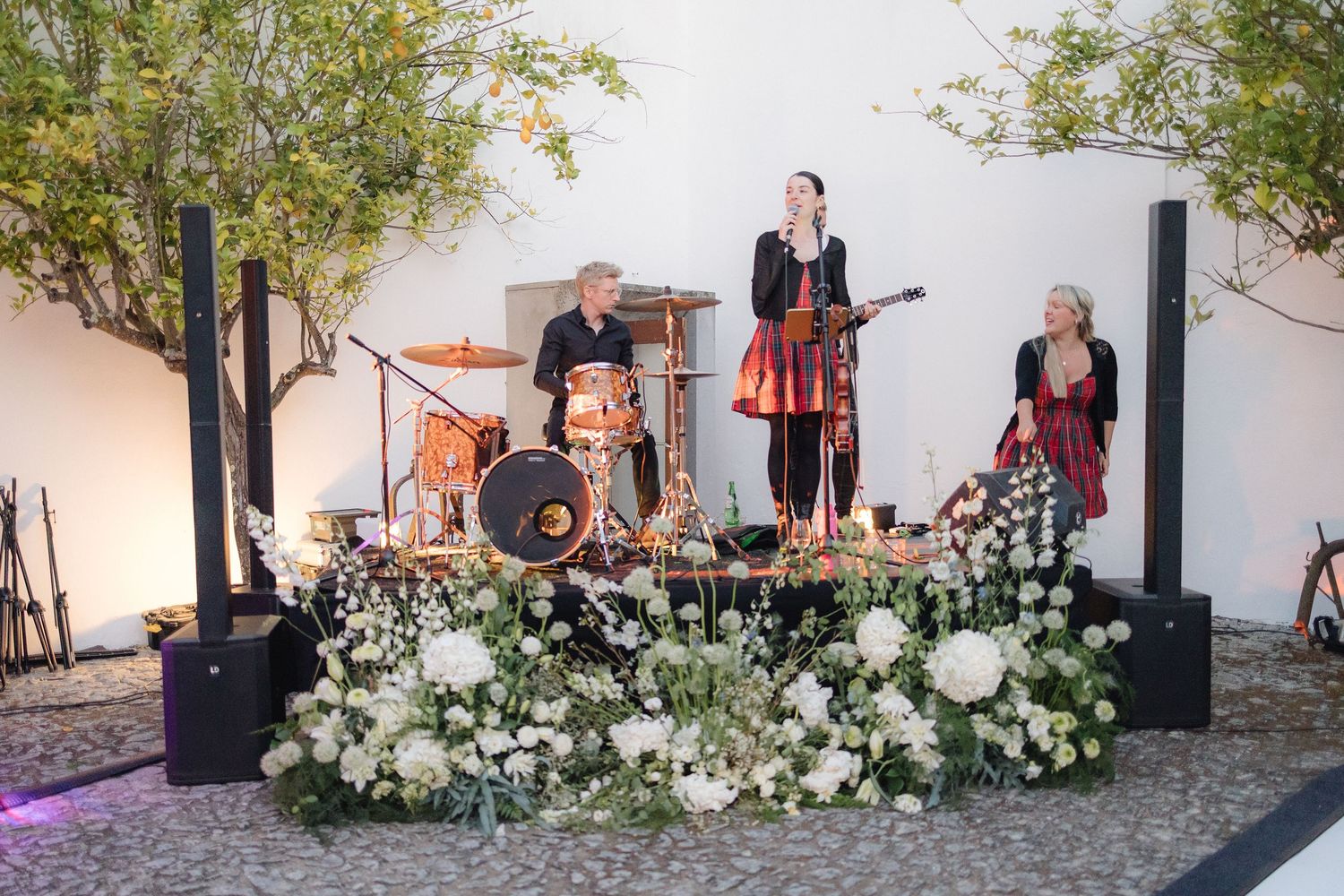 Live band performs at outdoor wedding reception with white floral arrangements and string lights.