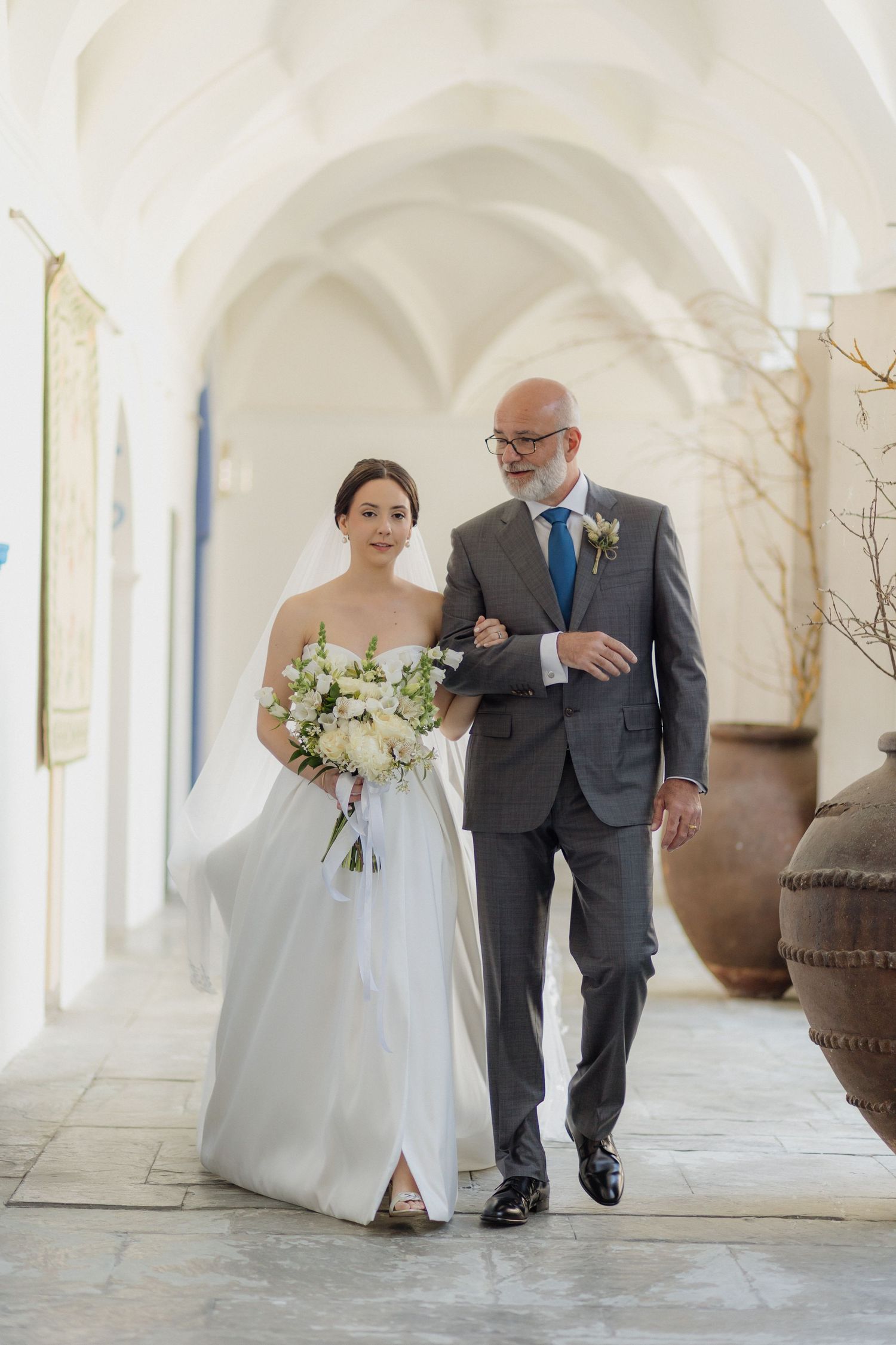 Traditional wedding processional in a bright white arched hallway.