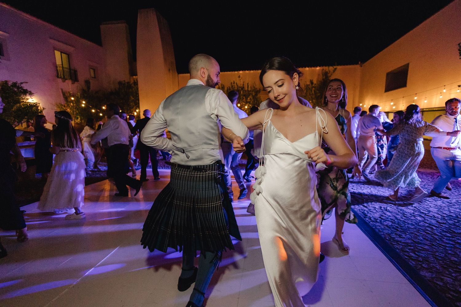 Wedding guests dancing on an illuminated dance floor during evening celebration.