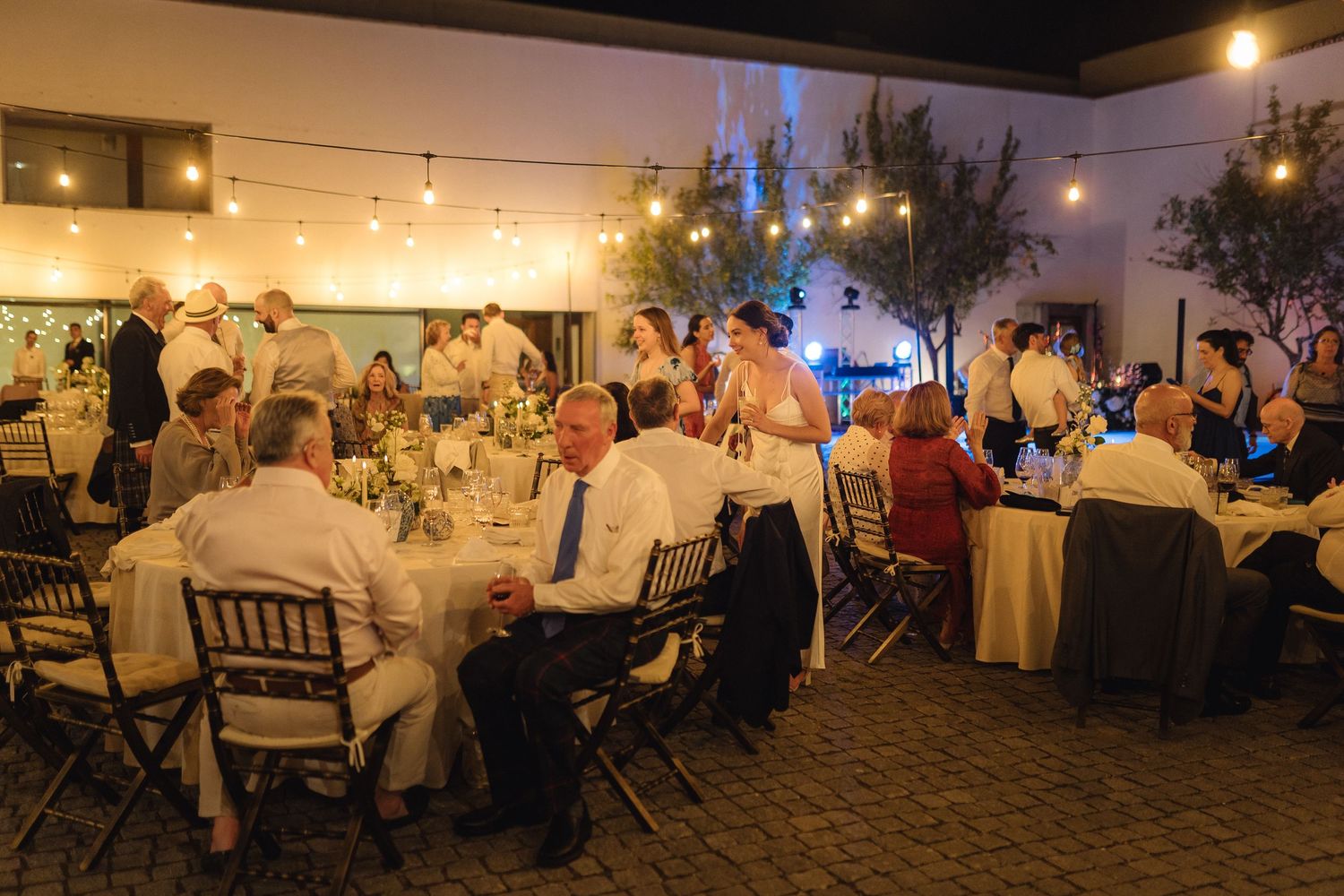 Wedding reception dining area with guests seated at round tables under ambient lighting.