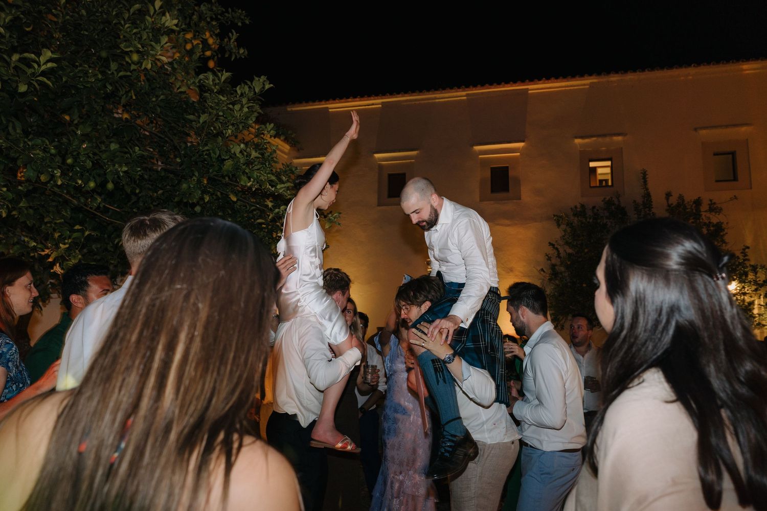 Wedding guests dancing and celebrating with raised arms at a nighttime reception.