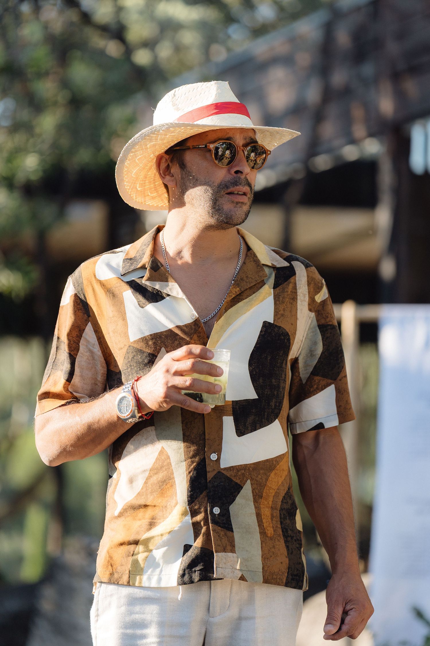 Guest in straw hat and patterned shirt enjoying outdoor wedding celebration.