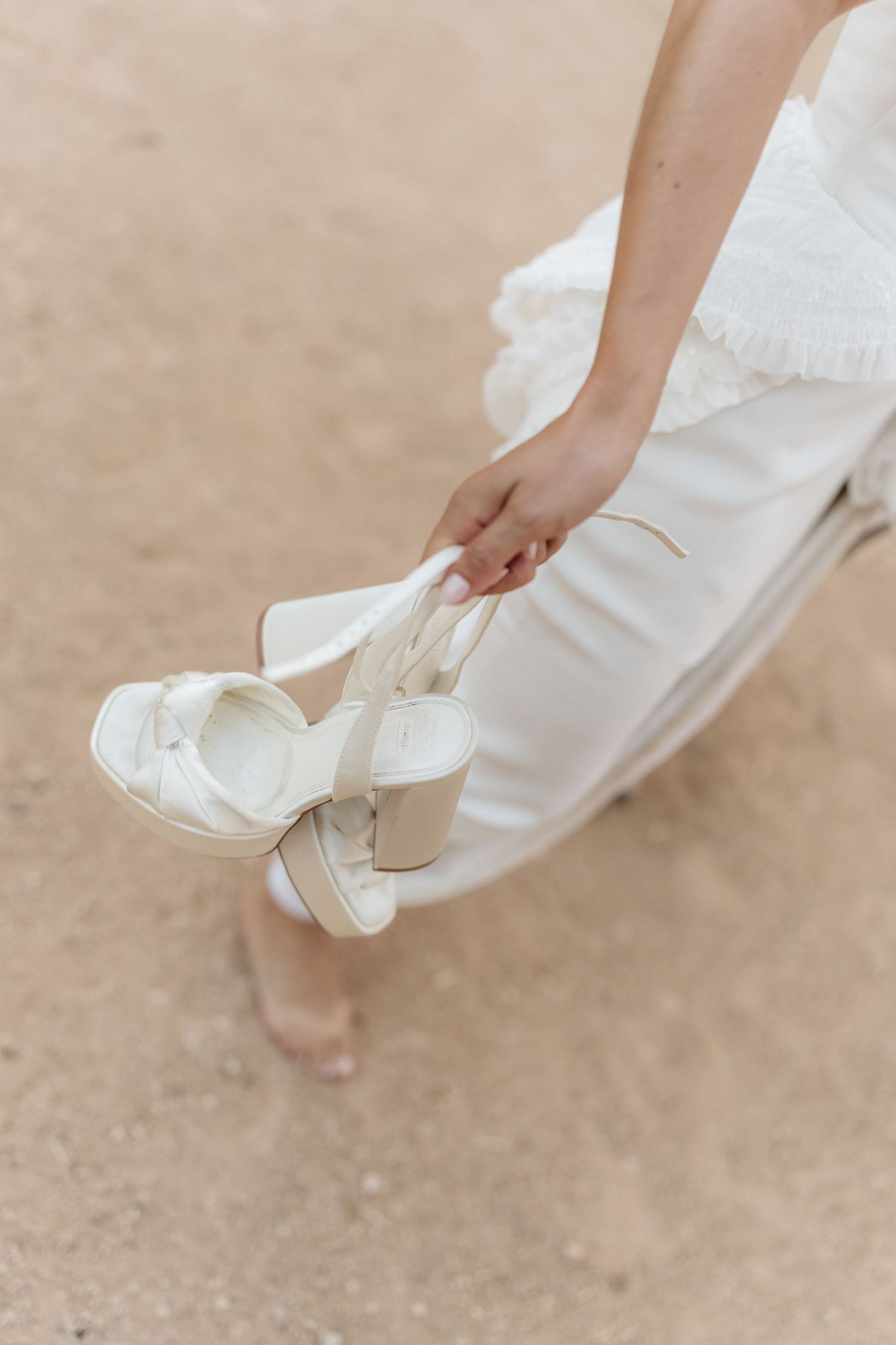 Close-up of white bridal shoes against a sandy ground.