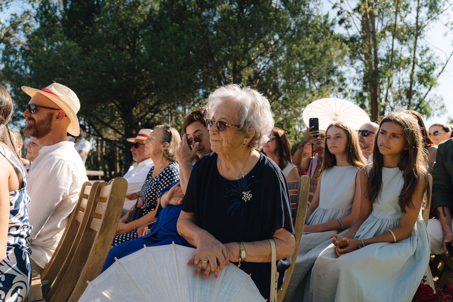 Wedding guests seated outdoors watching ceremony in natural setting.