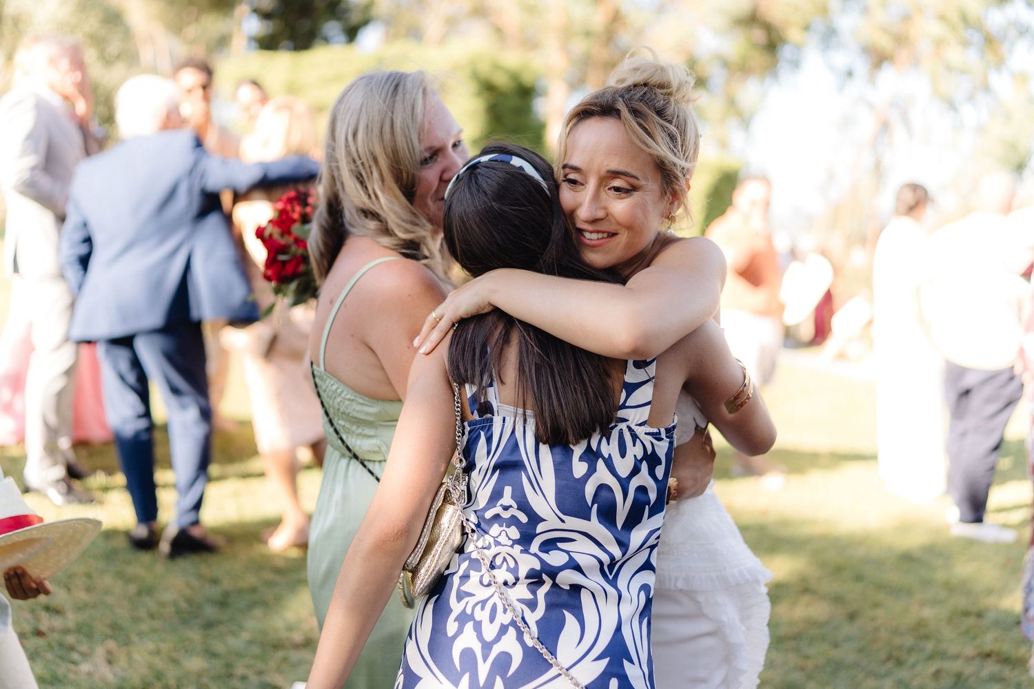 Wedding guests in navy patterned dresses embrace during outdoor celebration.