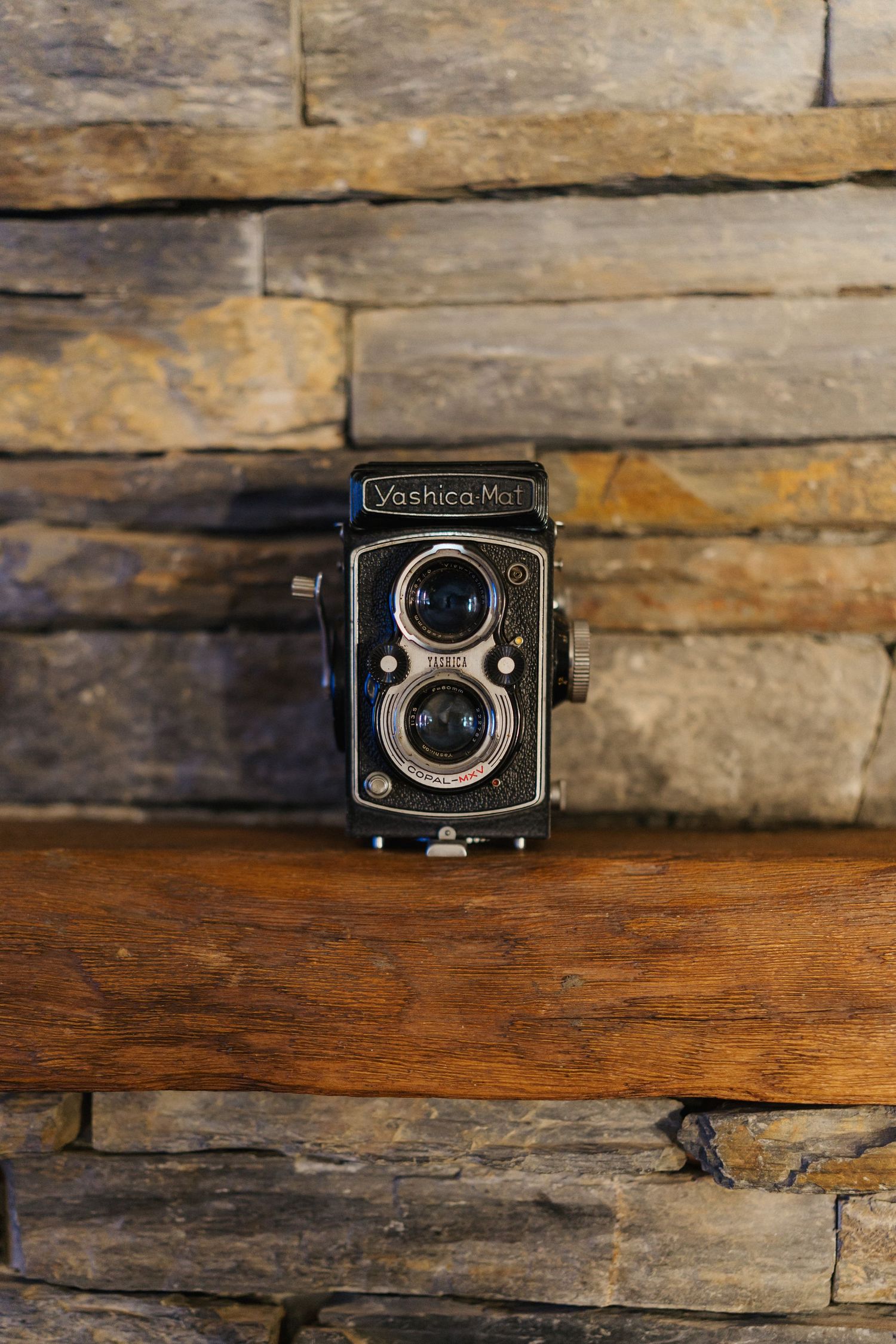 Vintage twin lens reflex camera displayed on rustic wooden shelf with stone wall background.