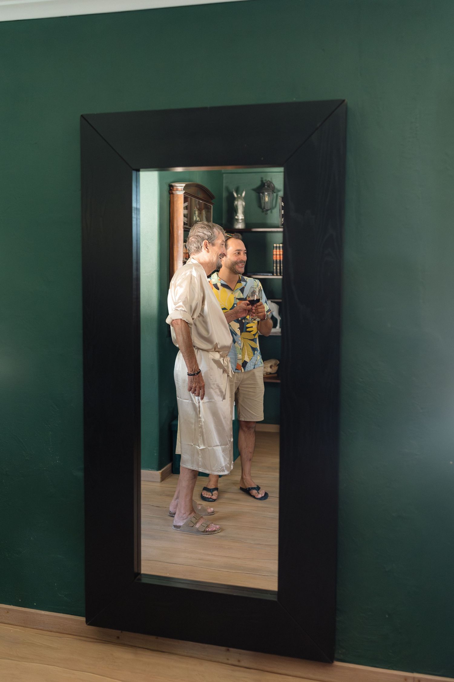 Reflection in a large black-framed mirror against a dark green wall showing interior scene.