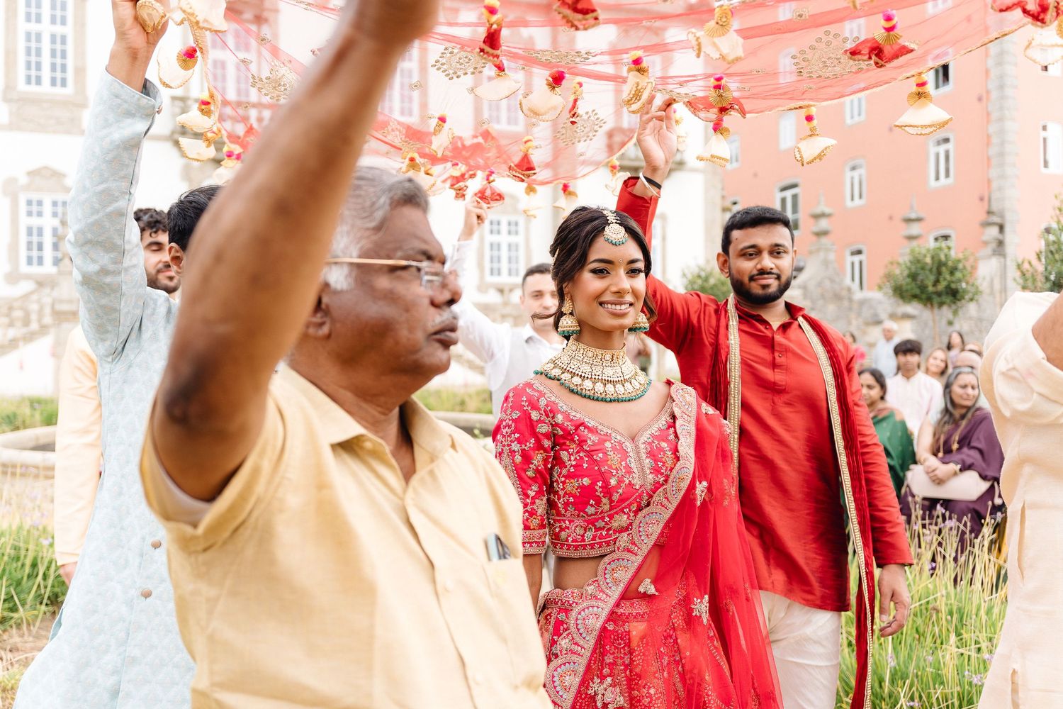 Festive celebration with people in traditional red and gold Indian attire dancing outdoors.