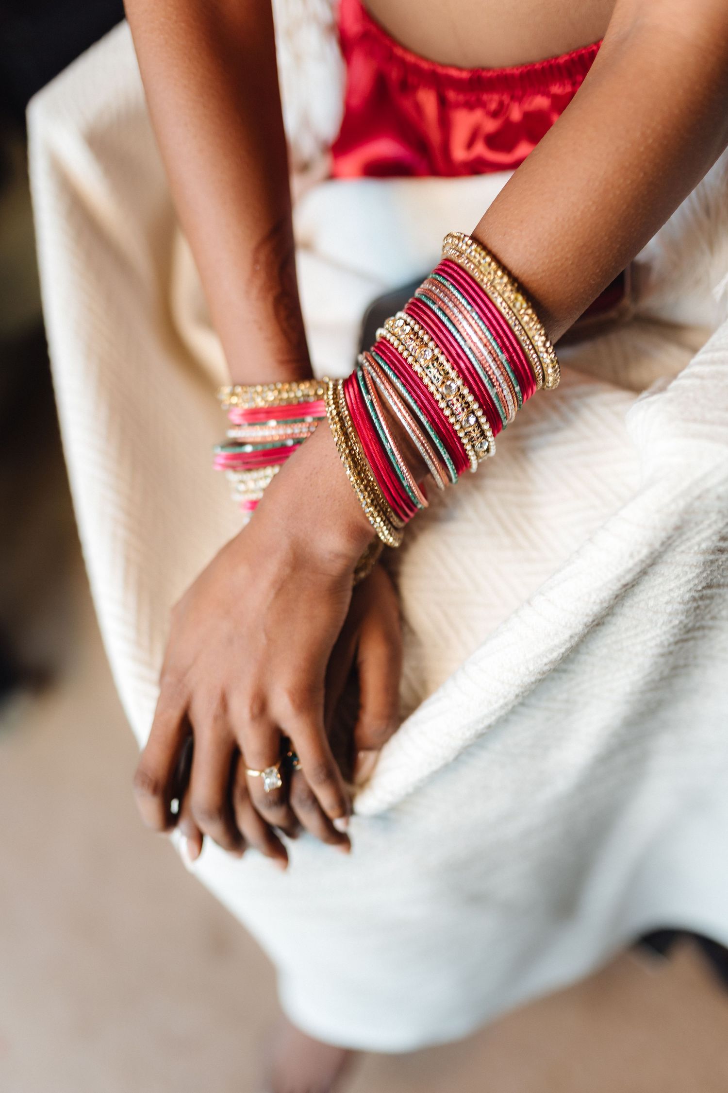 Traditional red and gold Indian wedding bangles and jewelry displayed on hands against white fabric.