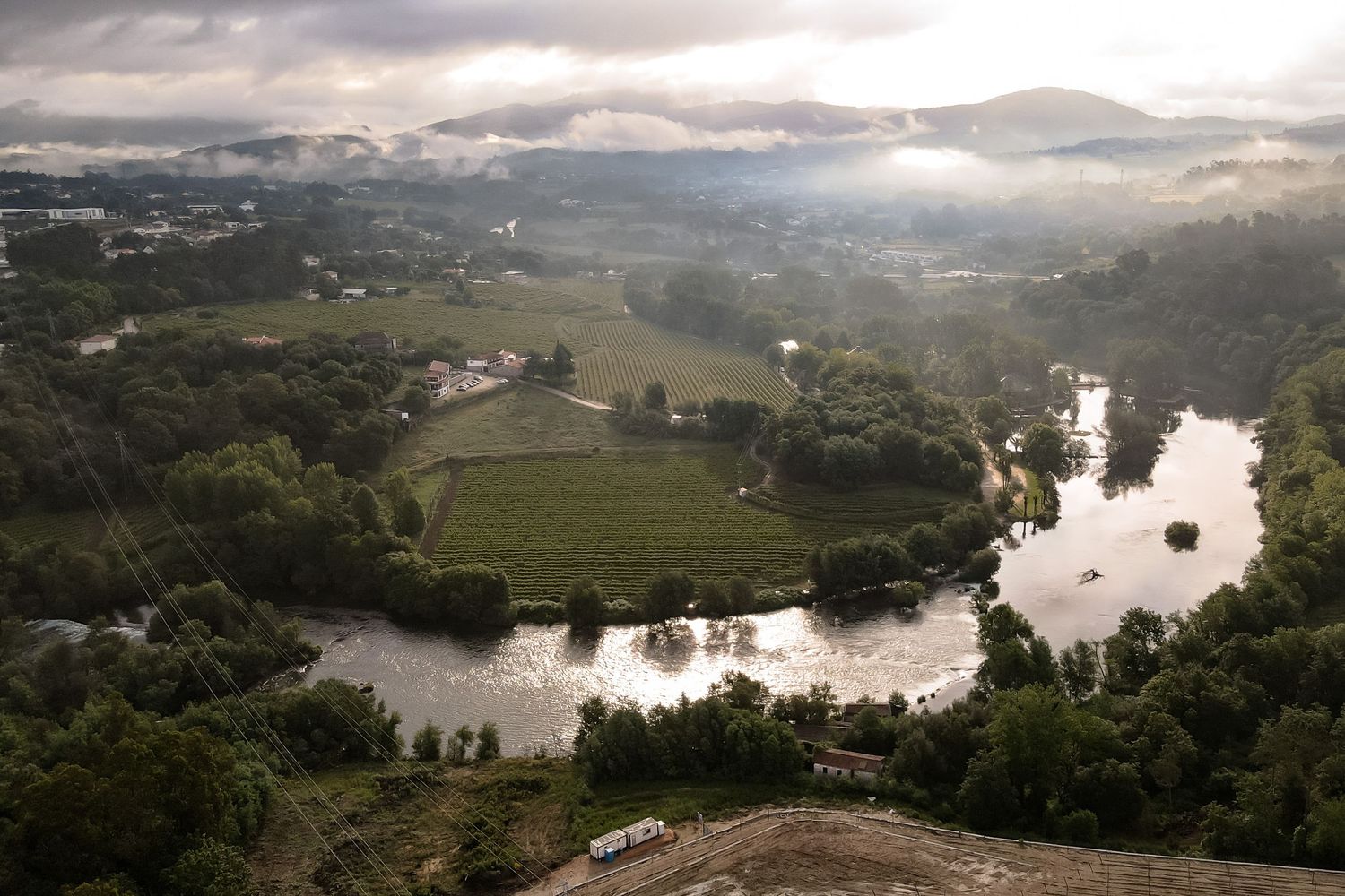 Panoramic aerial view of a winding river through lush green countryside with scattered buildings and cloudy skies.