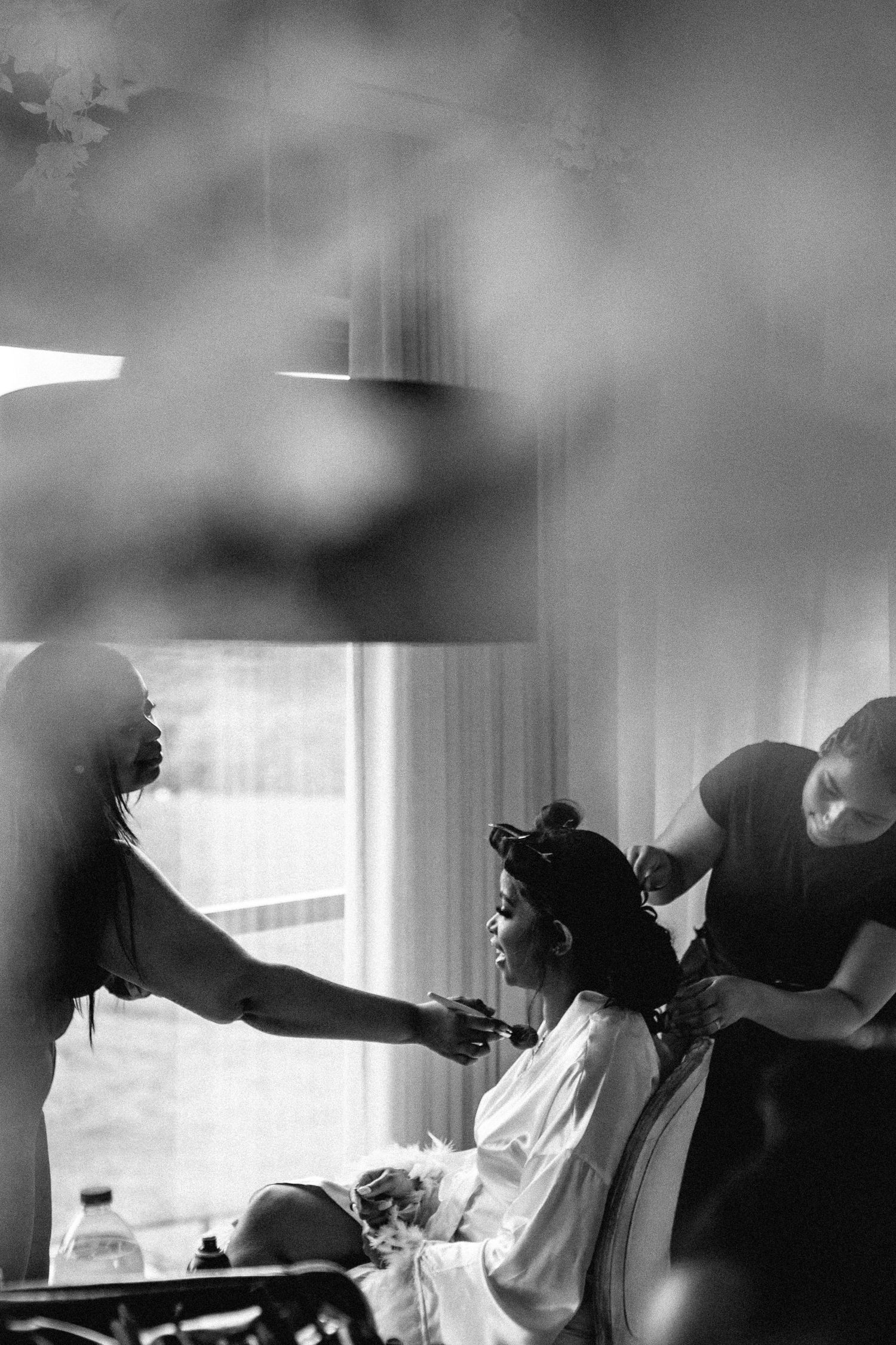 Black and white photo showing wedding preparations with stylists working on hair and makeup.
