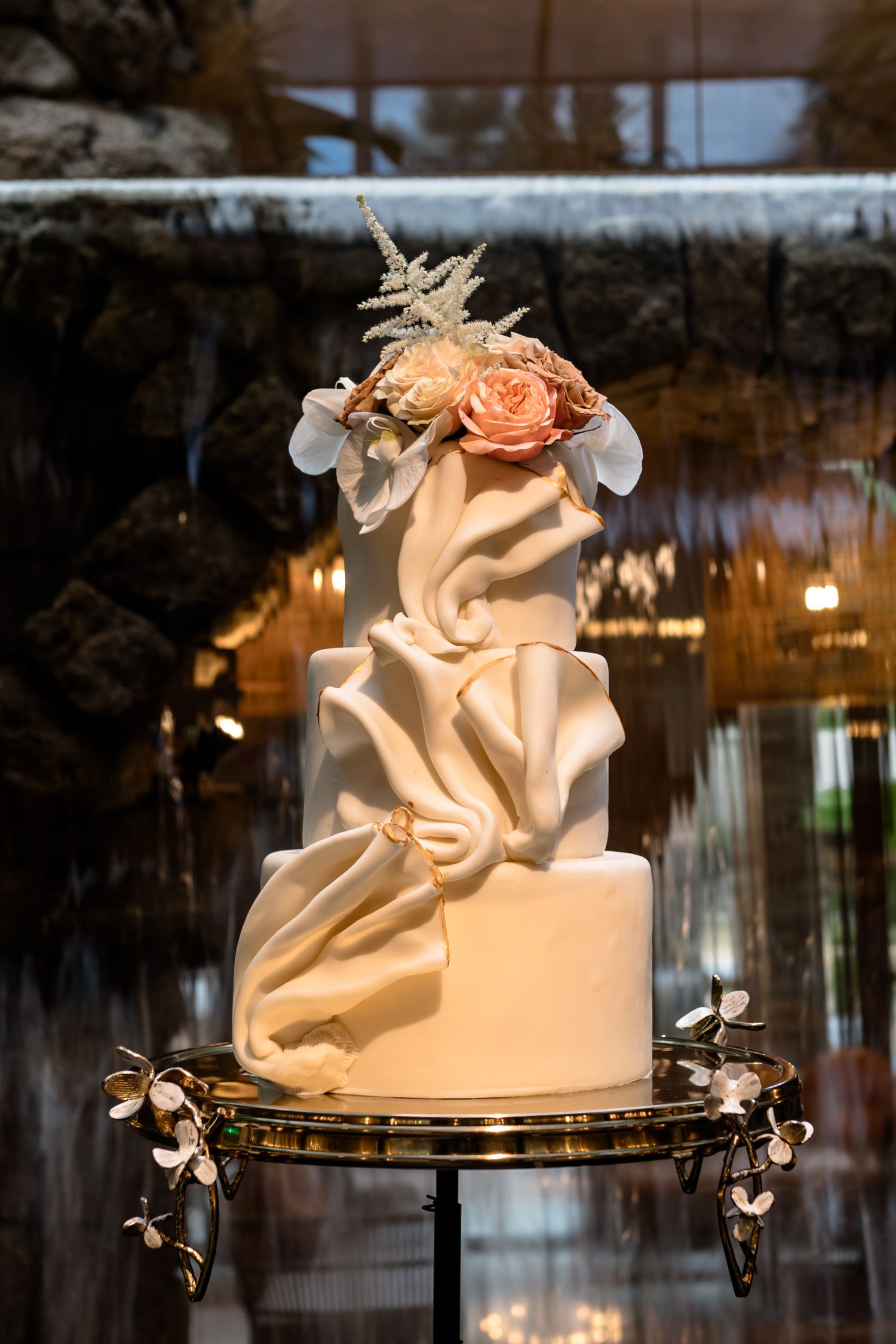 Elegant white wedding cake with draped fondant design and peach rose accents.