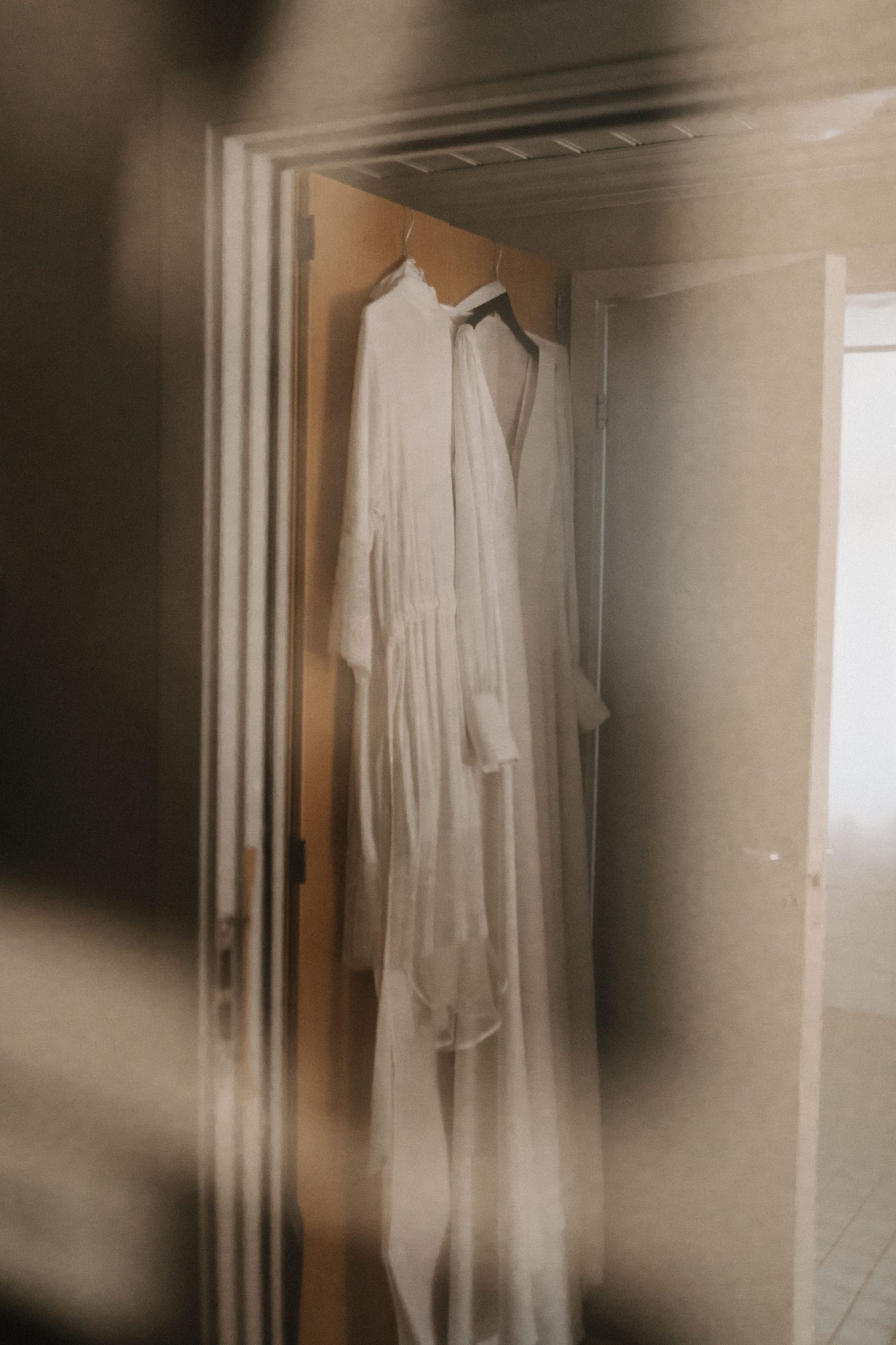 White wedding dress hanging in a softly lit room with dreamy, ethereal atmosphere.