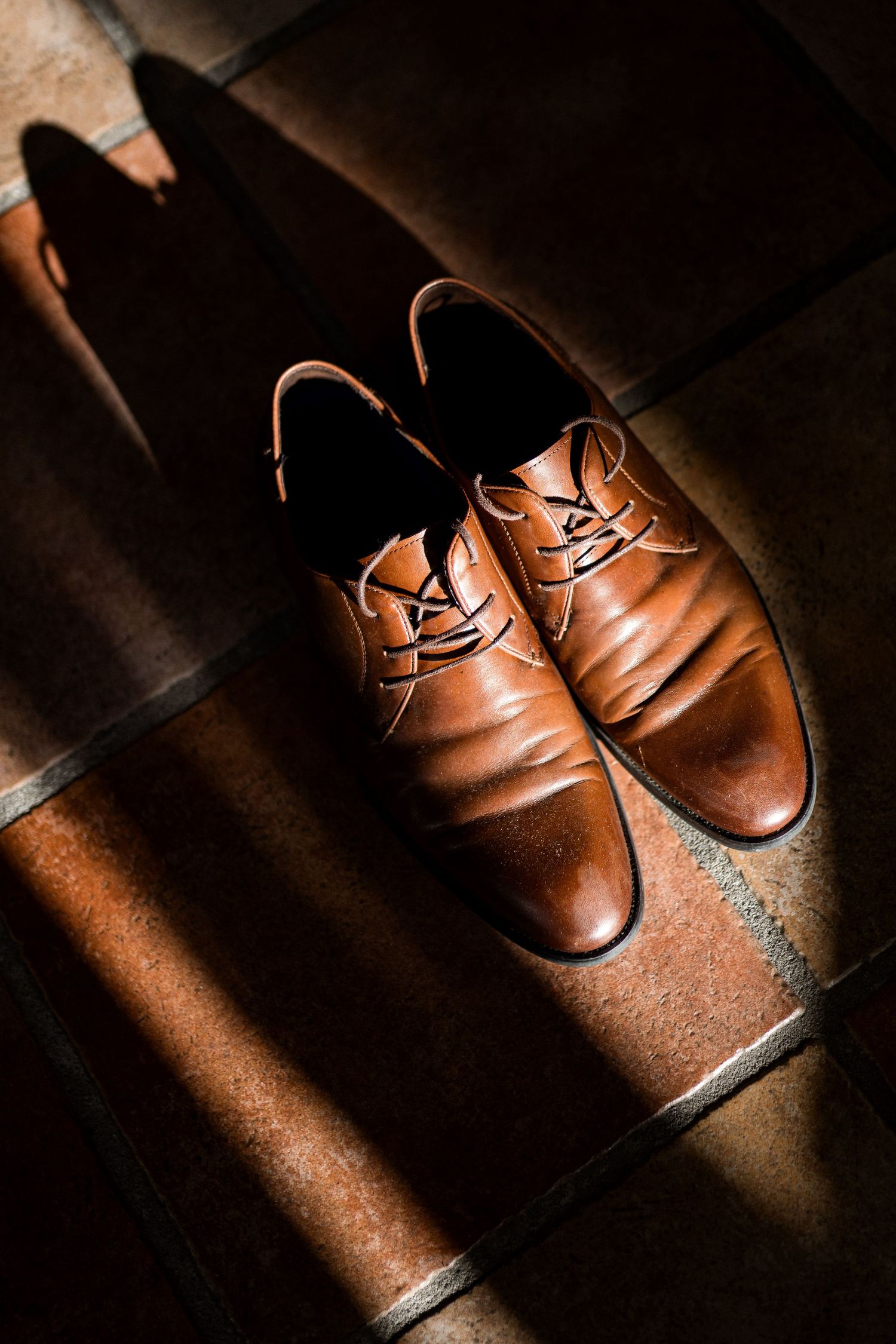 Brown leather dress shoes illuminated by dramatic lighting on a dark surface.