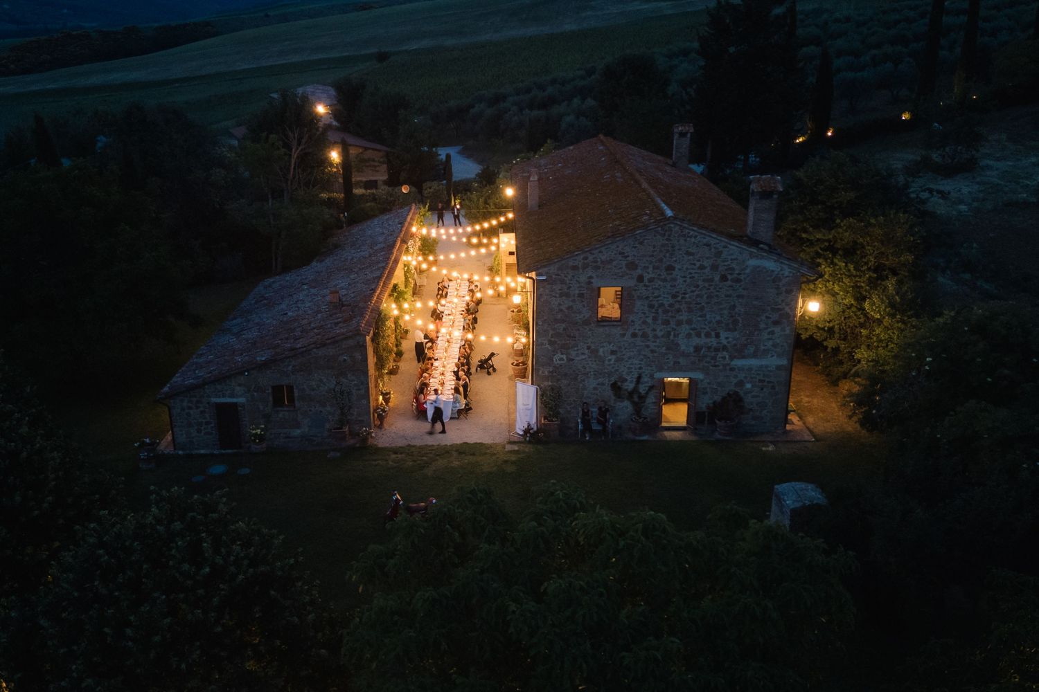 Aerial night view of rustic stone venue with string lights glowing during an outdoor wedding reception.