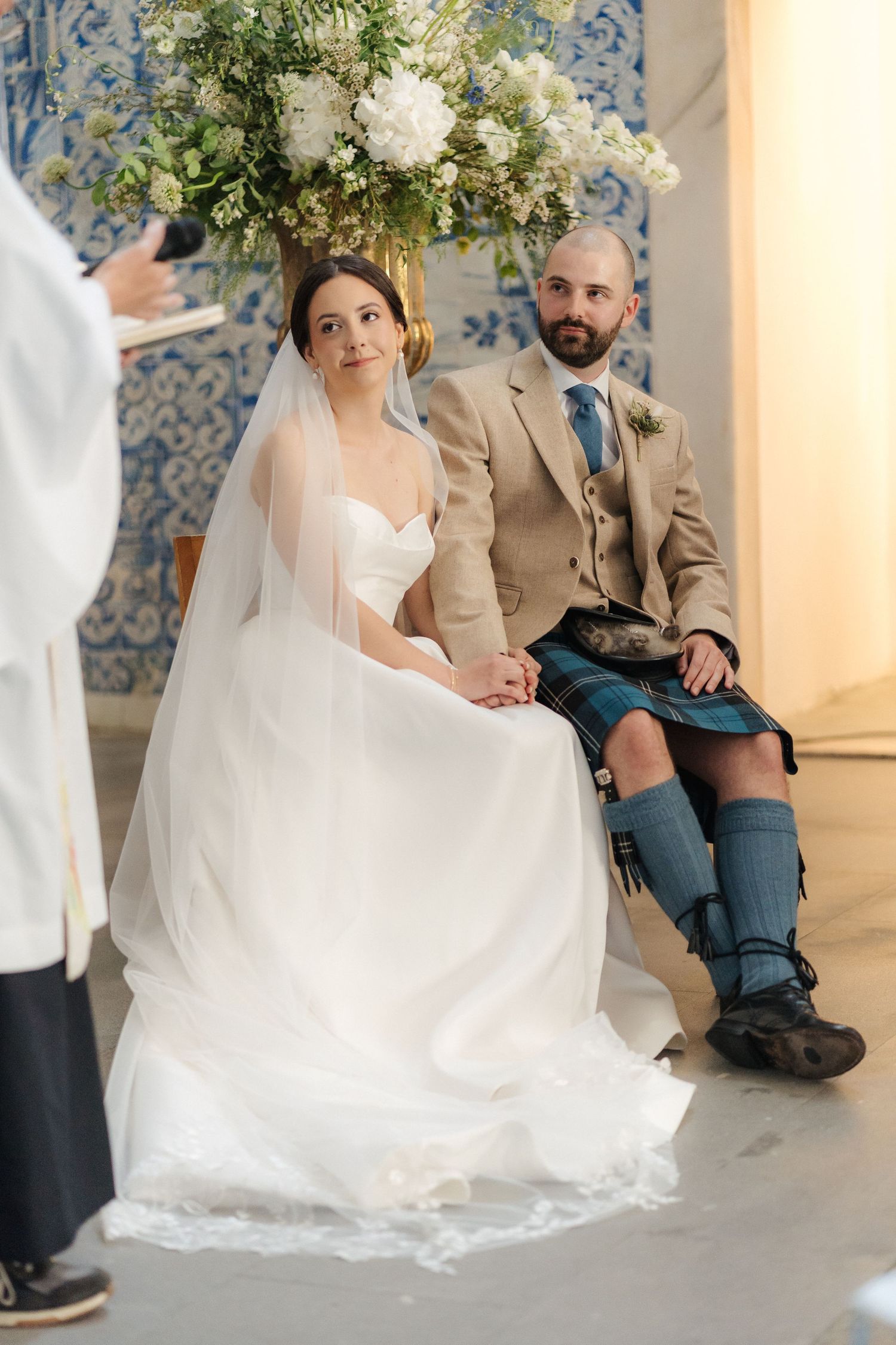 Elegant wedding ceremony in a chapel with ornate floral arrangements and Portuguese tile backdrop.