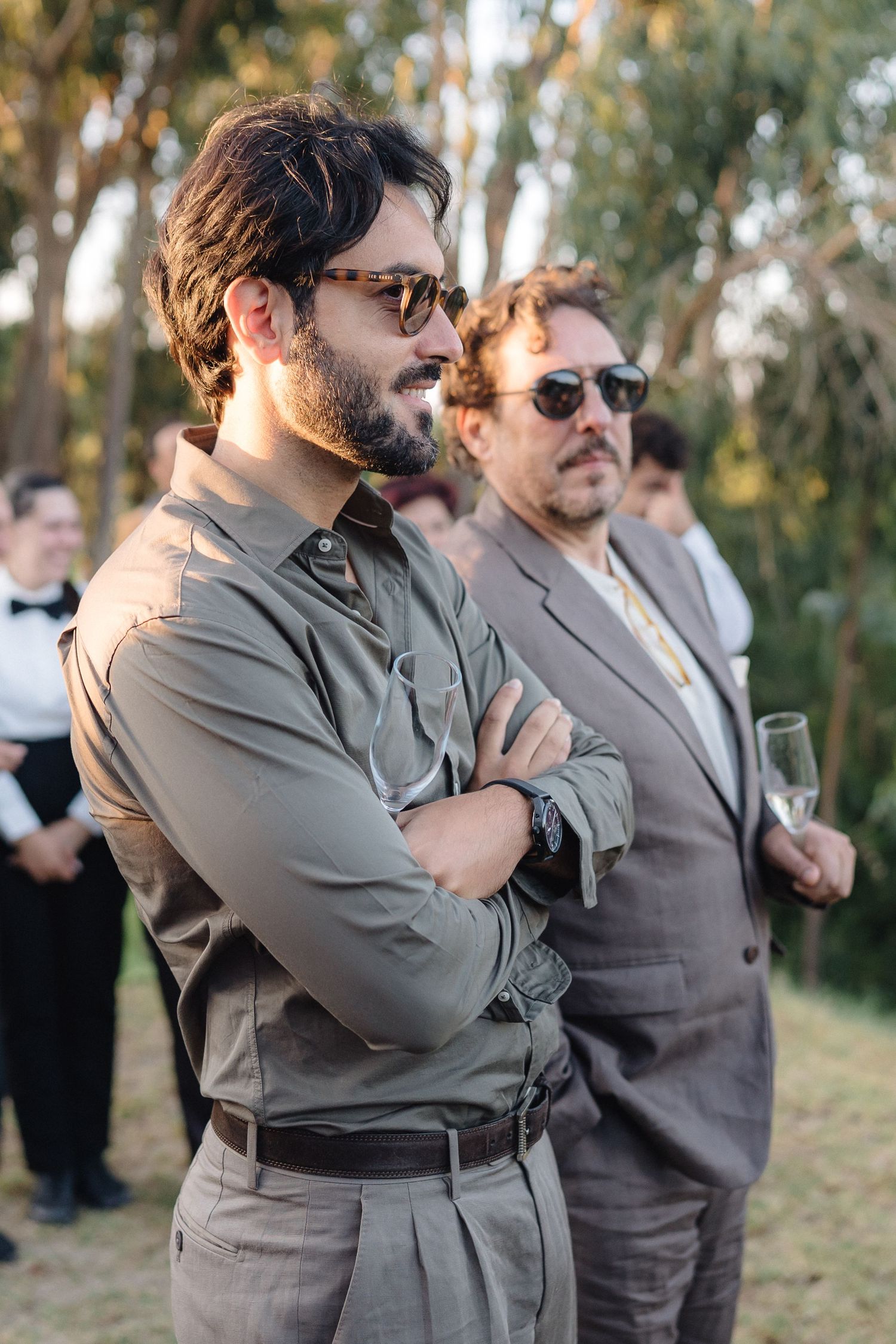 Wedding guests in gray suits embracing and celebrating during outdoor reception.