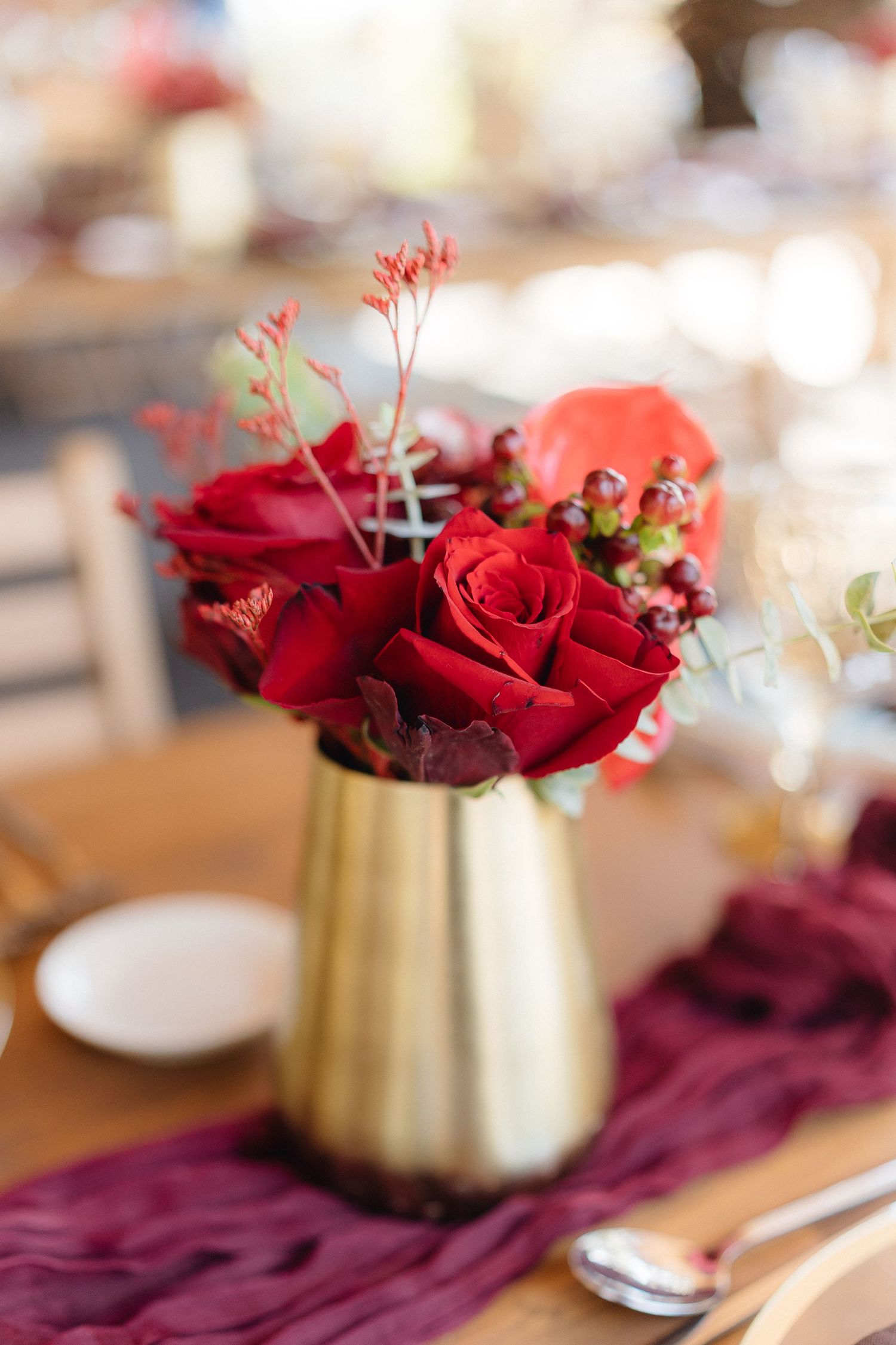 Deep red roses and floral arrangements in gold vases accent a burgundy table runner.