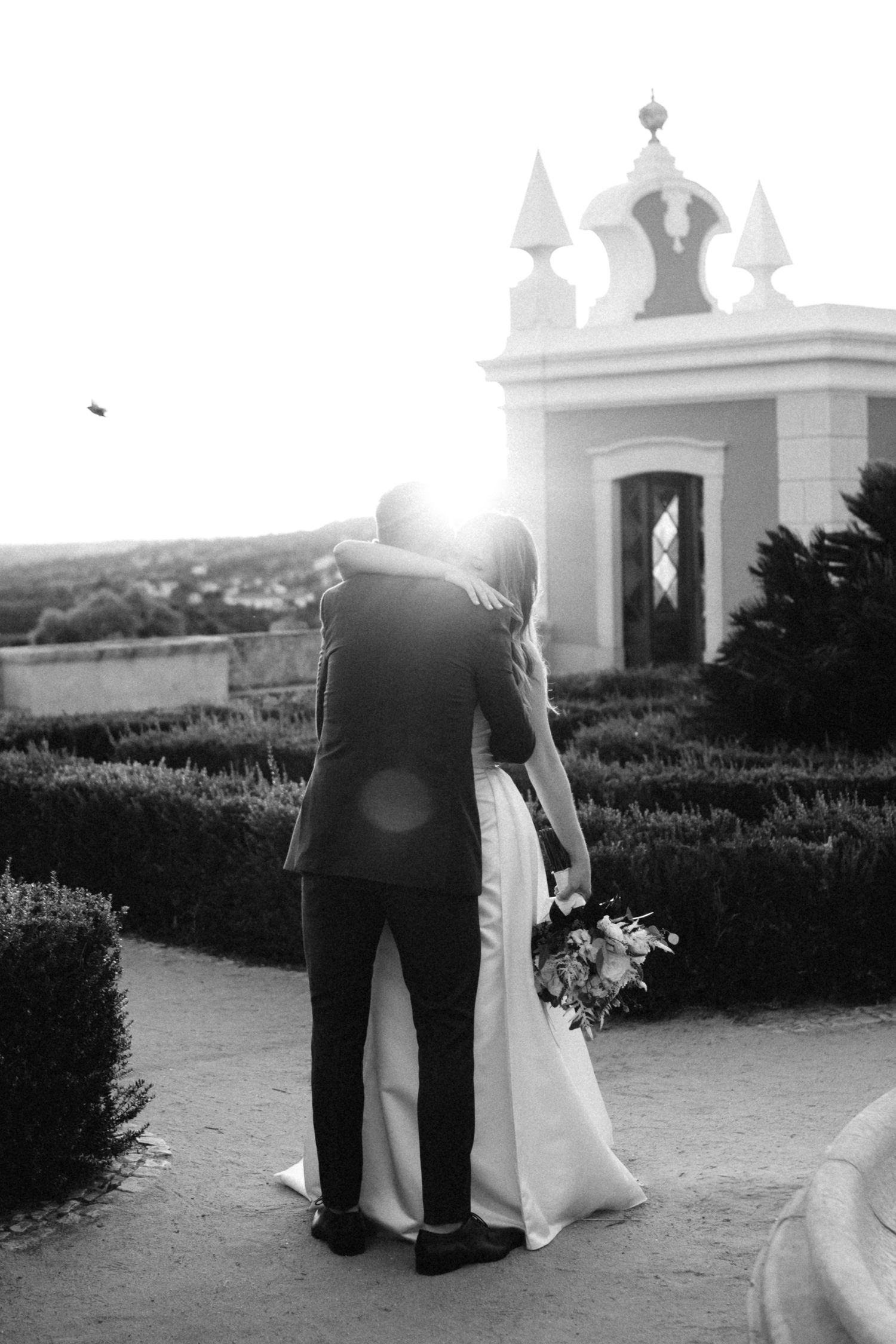 Romantic sunset wedding portraits in garden with architectural elements and dramatic lighting.