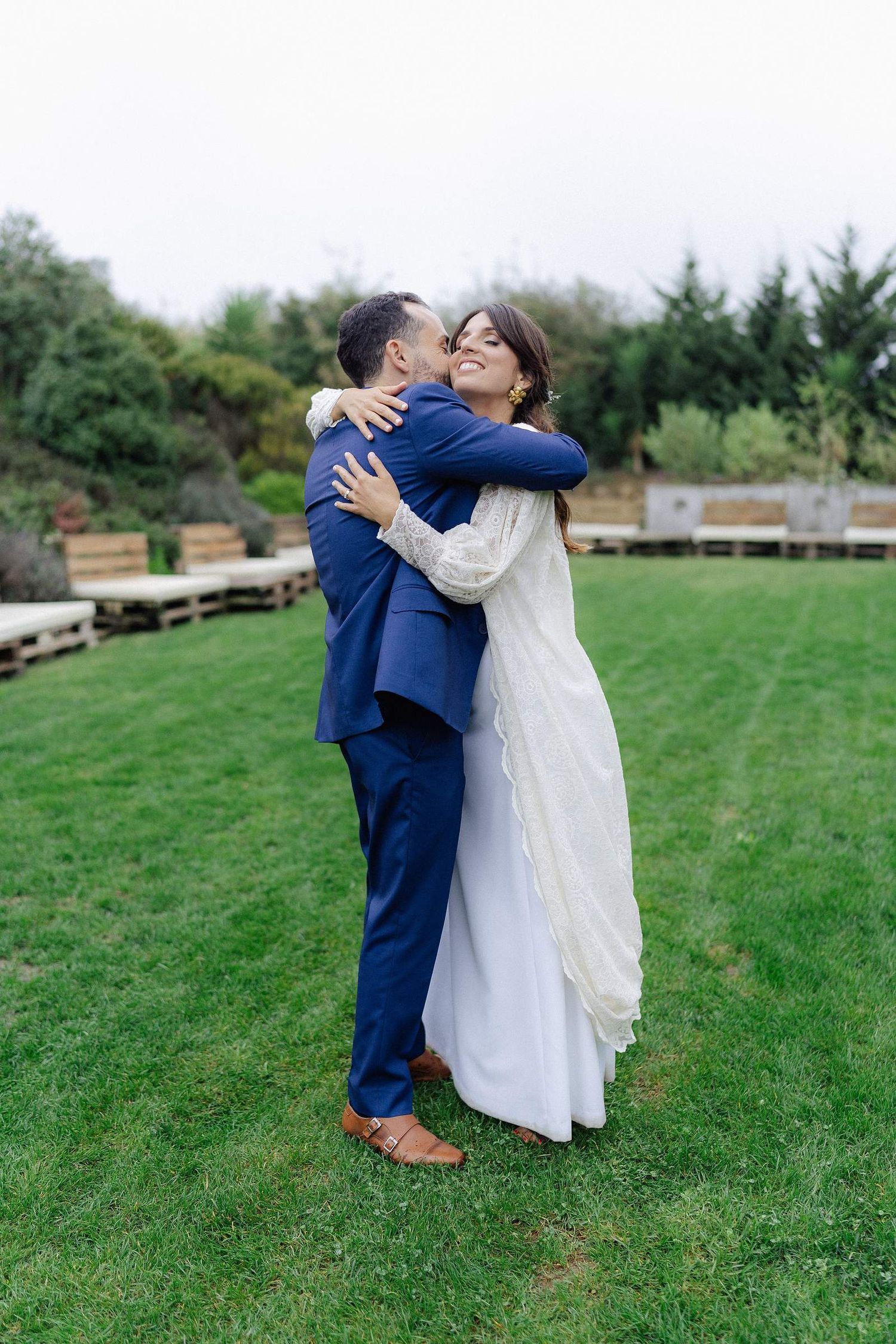Couple embraces joyfully on a green lawn during their wedding celebration.