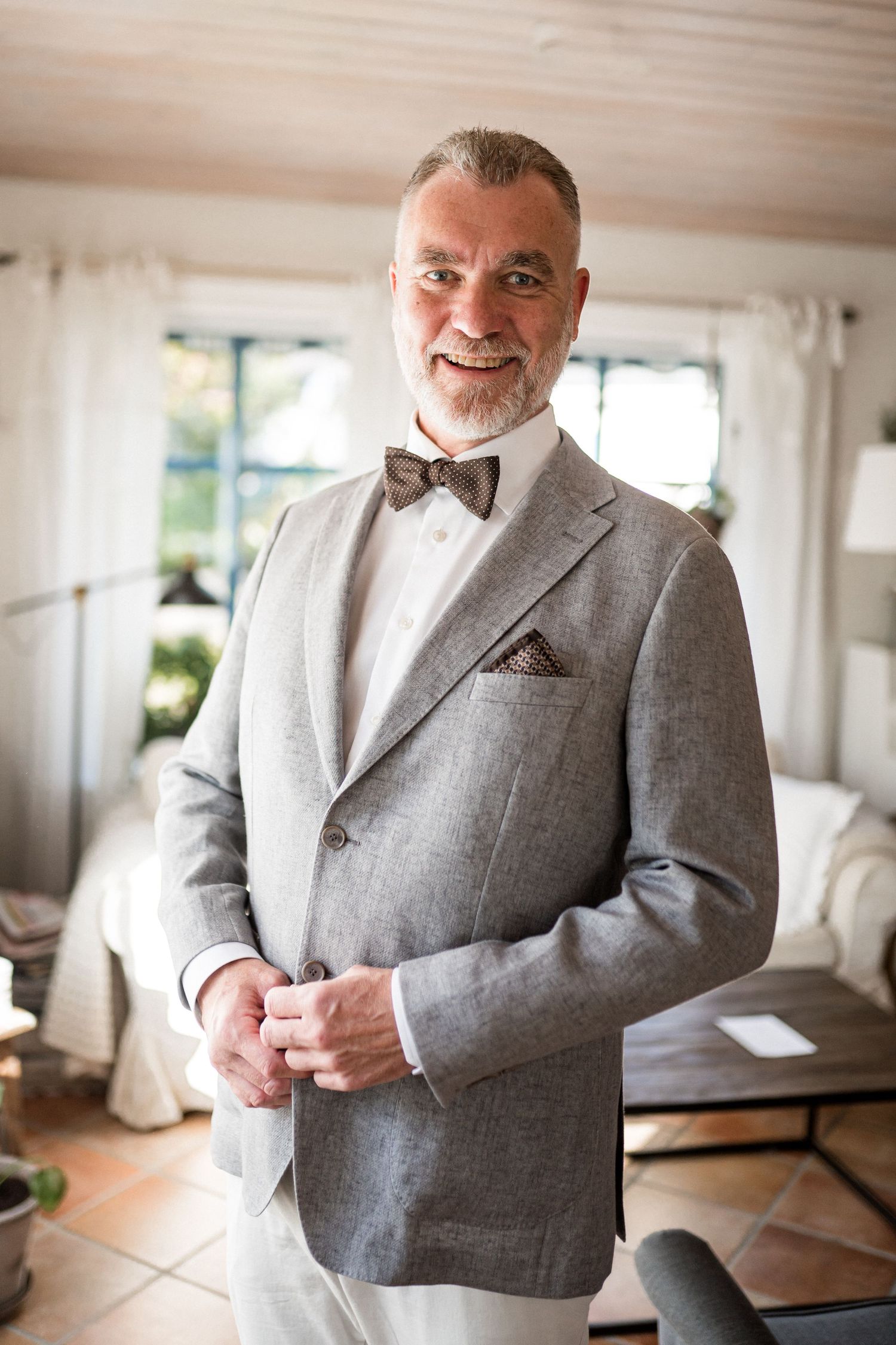 Person wearing a light gray suit jacket smiling in a bright interior space.