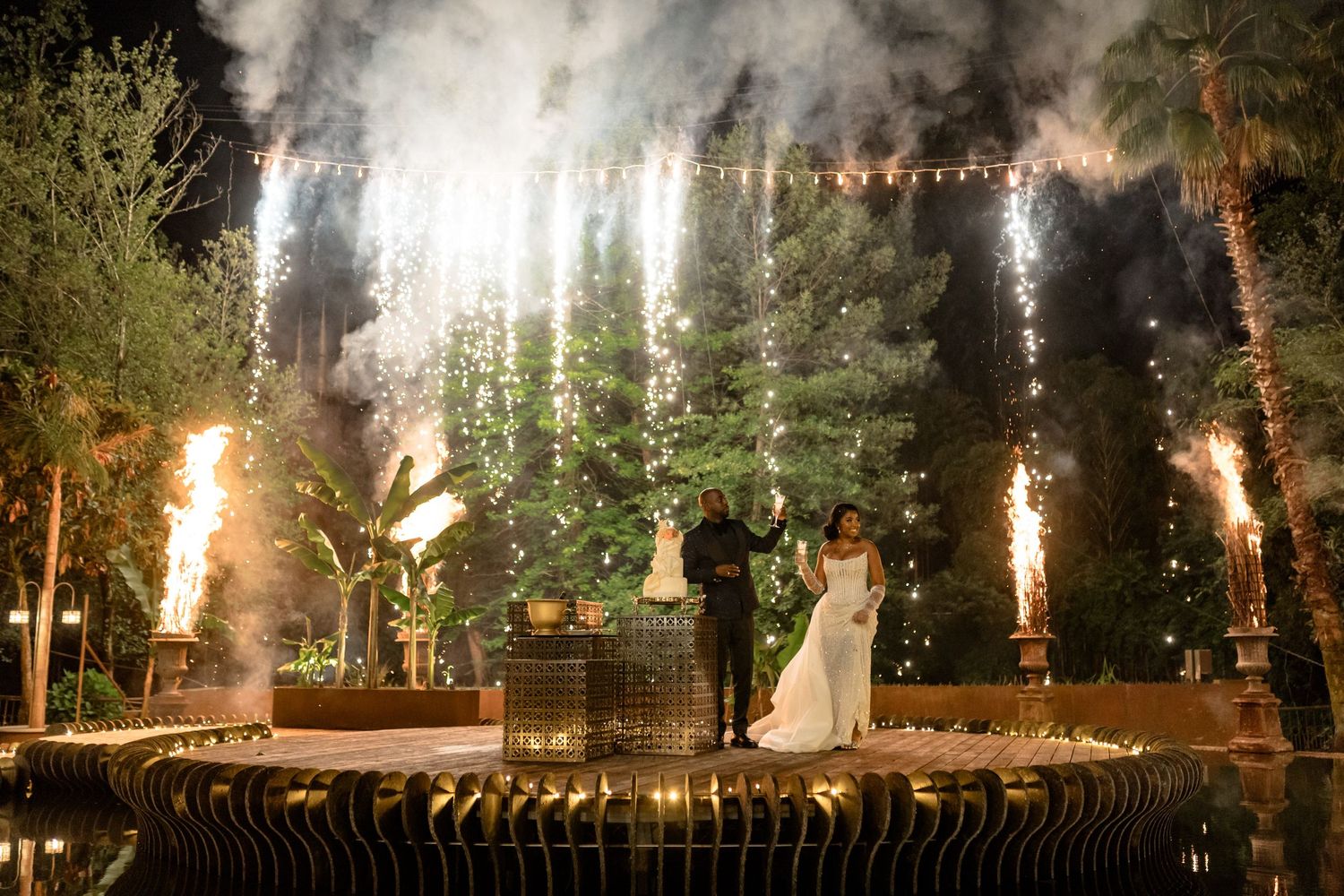 Outdoor wedding venue illuminated with string lights and dramatic smoke effects in a garden setting.