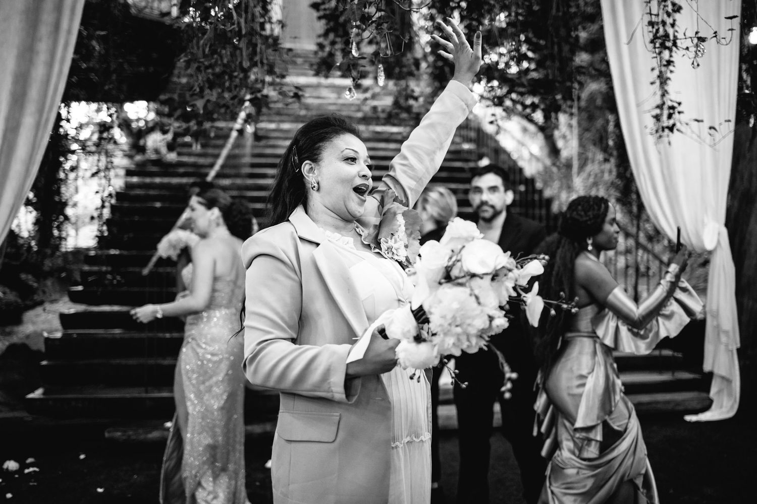 Outdoor wedding reception with guests mingling under trees and natural lighting.