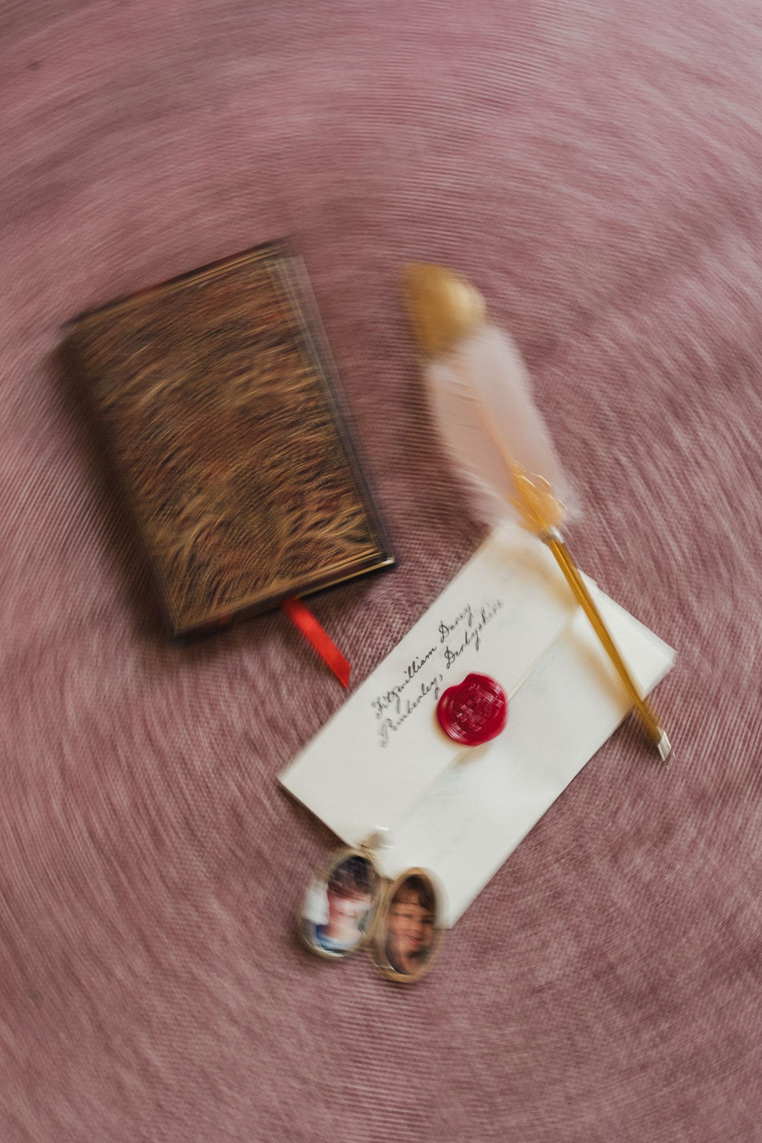 Wedding stationery with wax seals and feather quills arranged on a pink textured surface.