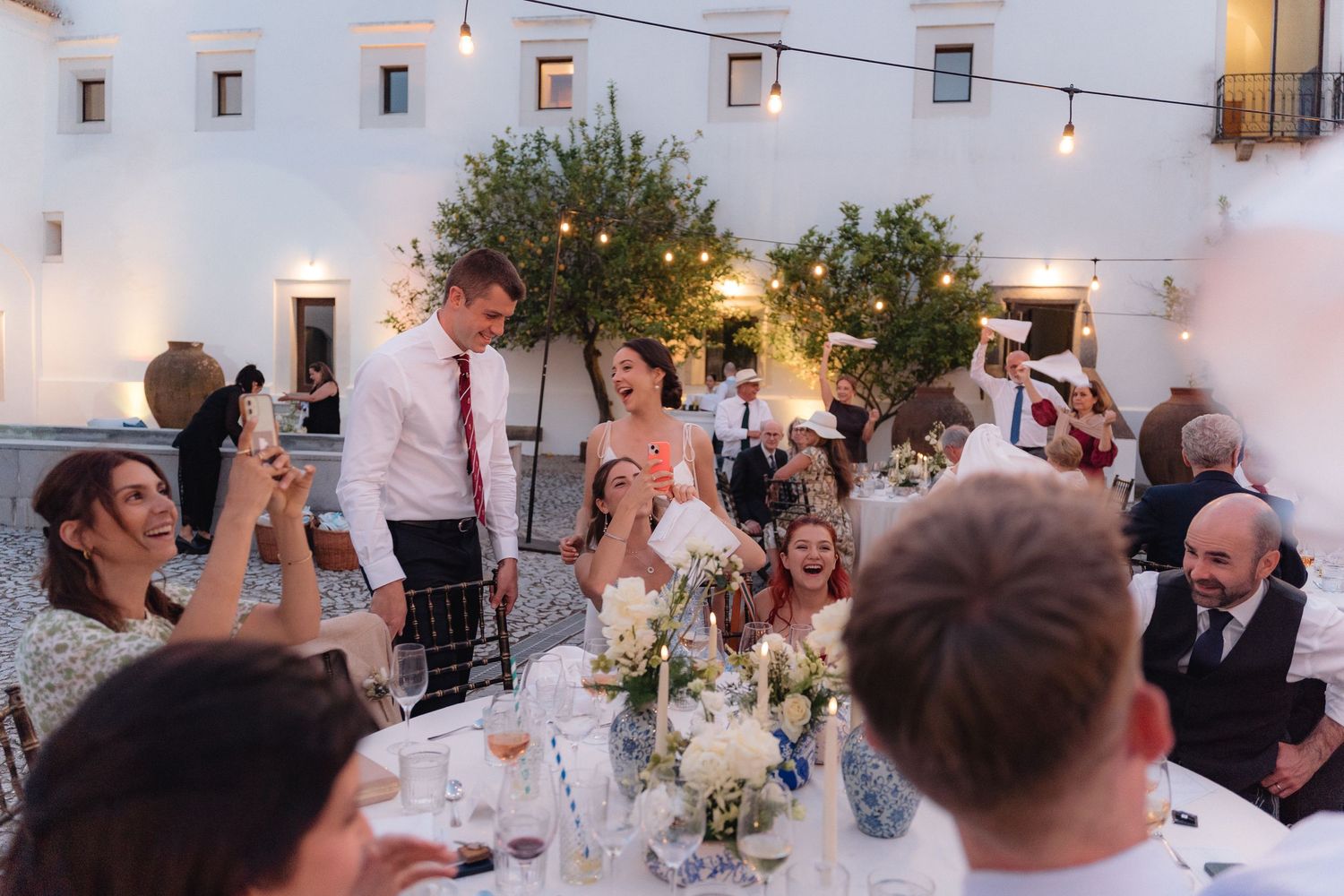 Evening wedding reception under string lights with white buildings and tables.