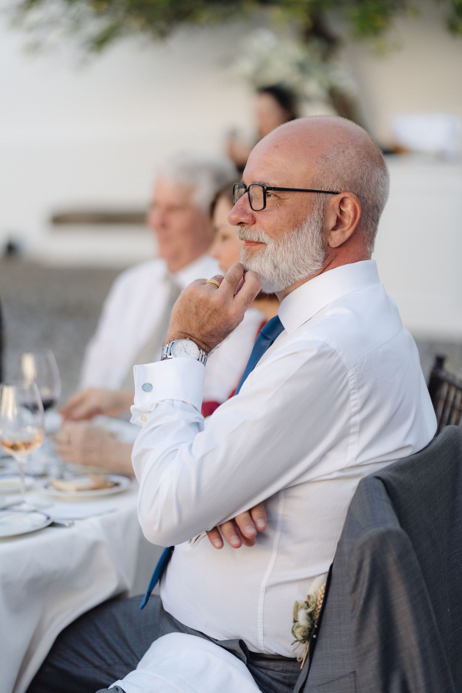 Guests in white dress shirts listening intently during outdoor dinner event.
