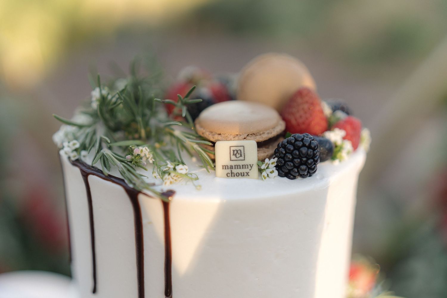 Elegant white wedding cake with dripping chocolate and fresh berries on display.
