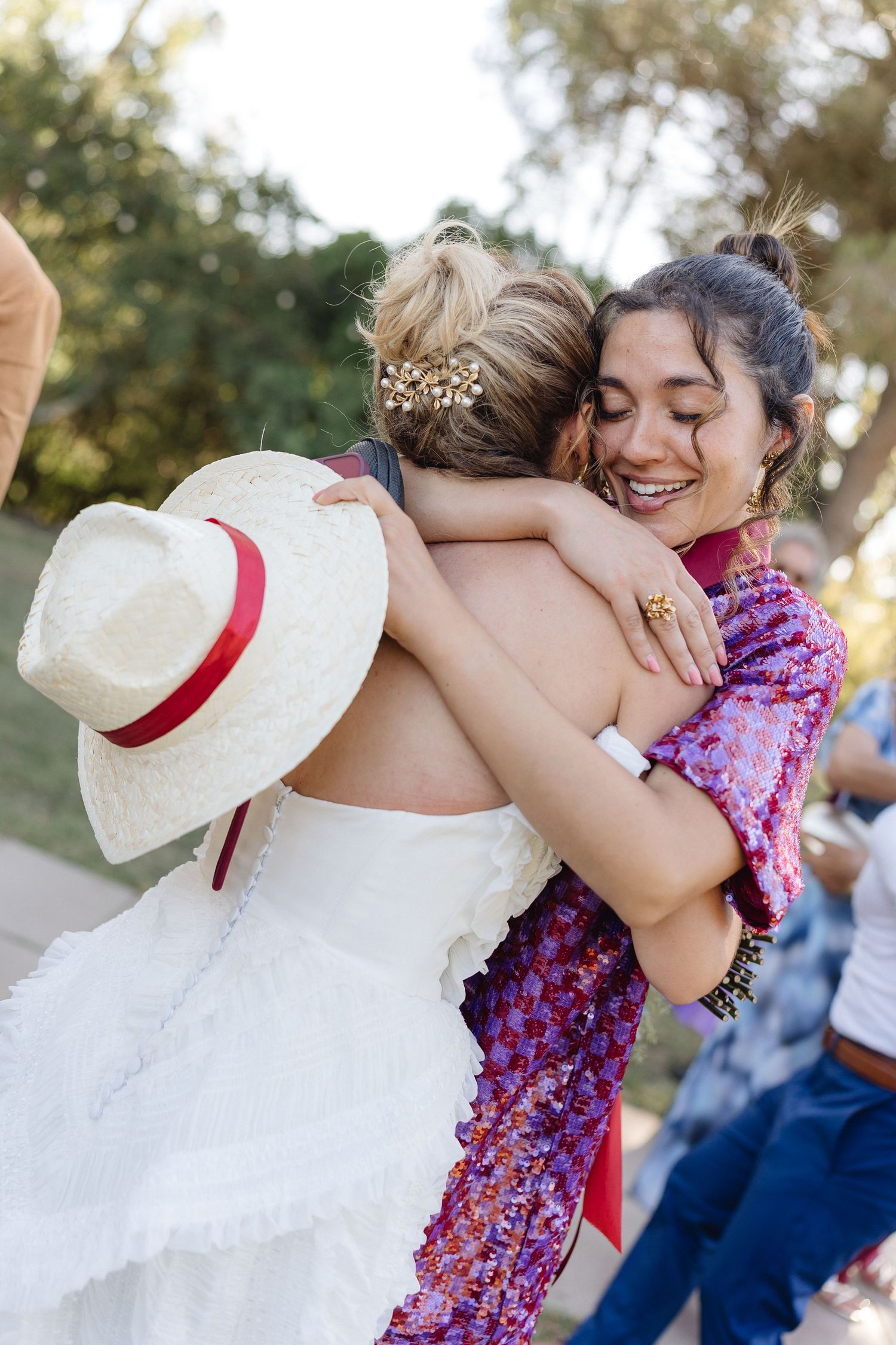 Two guests share an emotional embrace at an outdoor wedding celebration.