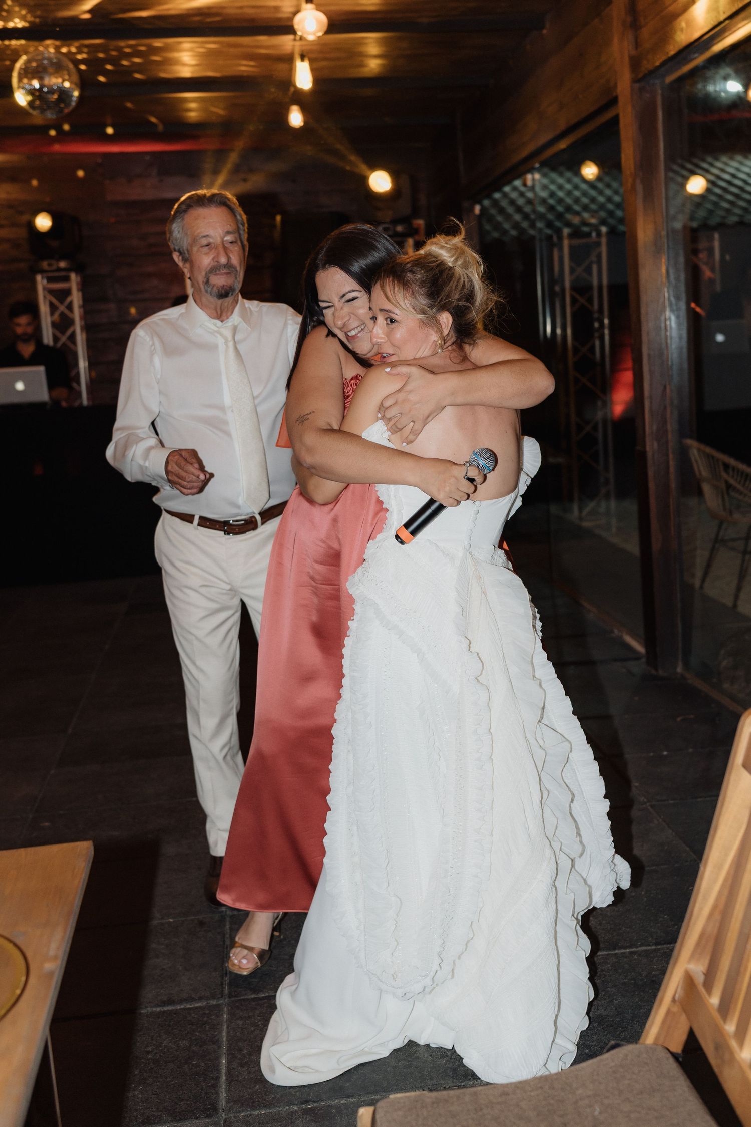 Wedding celebration with guests dancing and embracing on a patio under string lights.