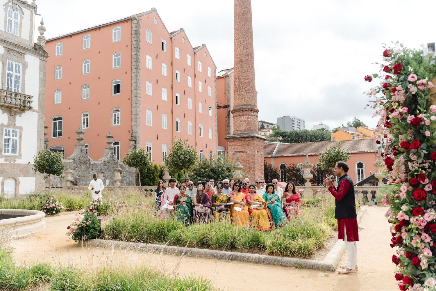Panoramic view of a brick building exterior with landscaped grounds and gathered wedding guests.