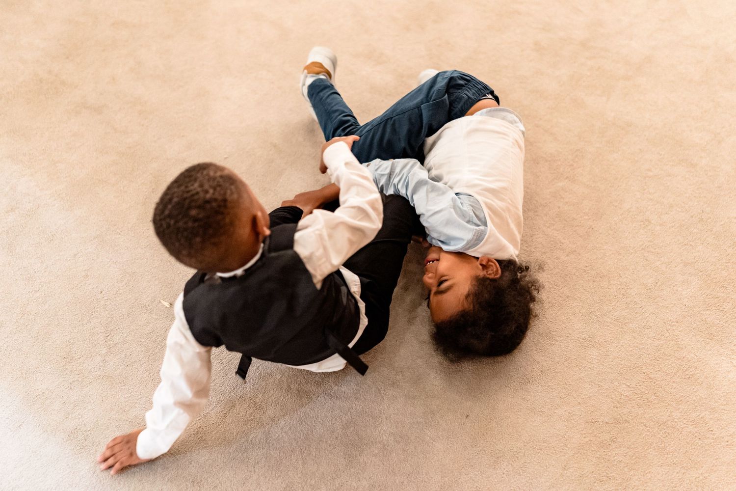 Aerial view of two young children playing on beige carpet.