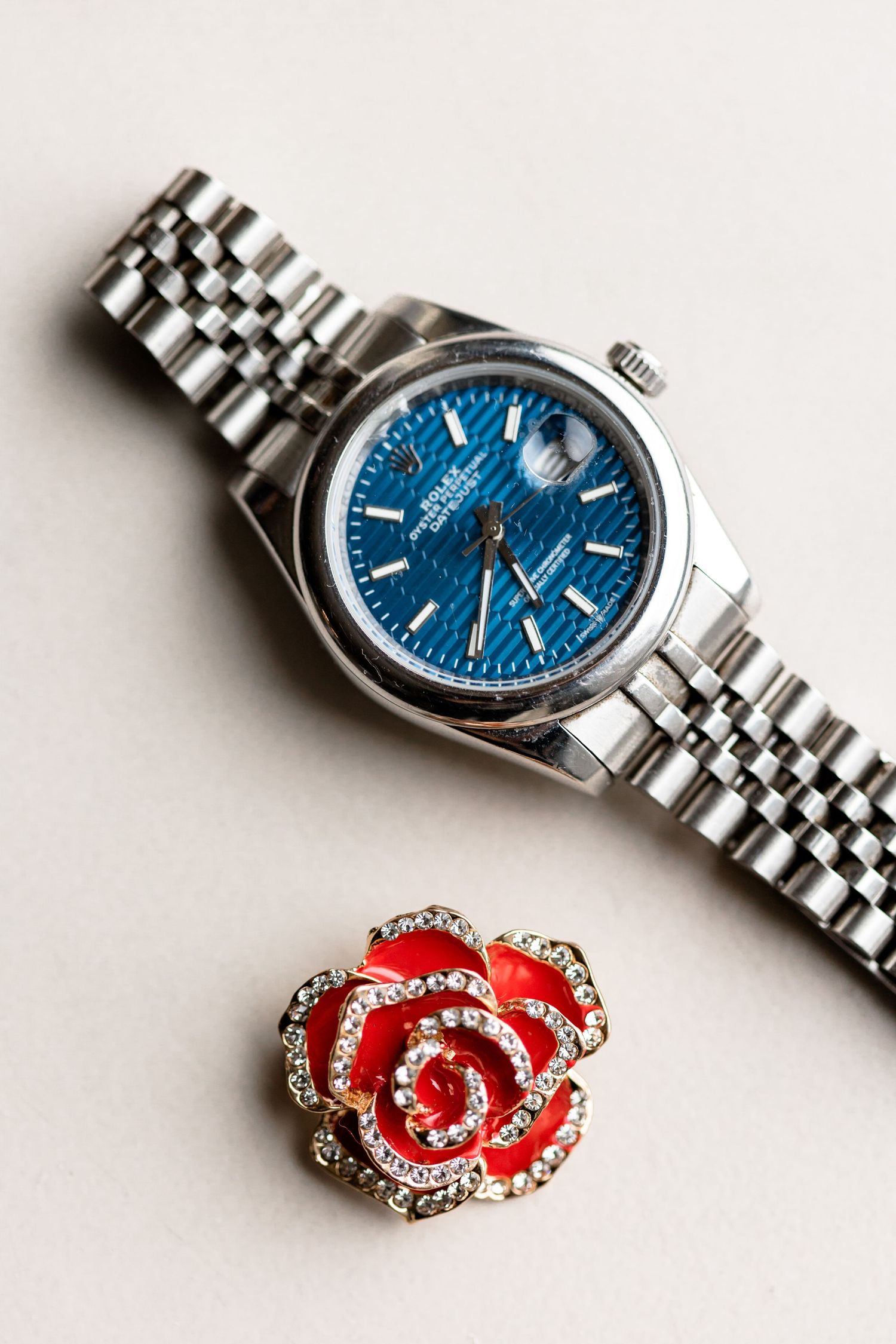Silver watch with blue dial face and red crystal rose brooch on white surface.
